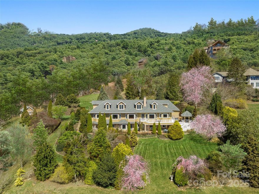Overlooking the 11th fairway of Laurel Ridge Country Club, this exquisite English-style country estate spans over 3 acres, offering breathtaking 20-mile ridgeline mountain views. Designed for both serene luxury and effortless entertaining, the home features a spacious gourmet kitchen and a seamless blend of indoor and outdoor living spaces, perfect for year-round enjoyment. The main level boasts a sophisticated study, ideal for a home office, and a lavish primary suite with two walk-in closets and a spa-like bath adorned with elegant blonde onyx tile and heated floors. Upstairs, a comfortable family room, guest suite, and flex room provide ample space for relaxation. The terrace level offers a private retreat with two guest suites, a cozy den, a hobby room, and additional bonus room. Outside, the meticulously maintained level yard is a gardener’s paradise, showcasing vibrant flowers, lush trees, & a tranquil stream. This exceptional property is just minutes from downtown Waynesville.