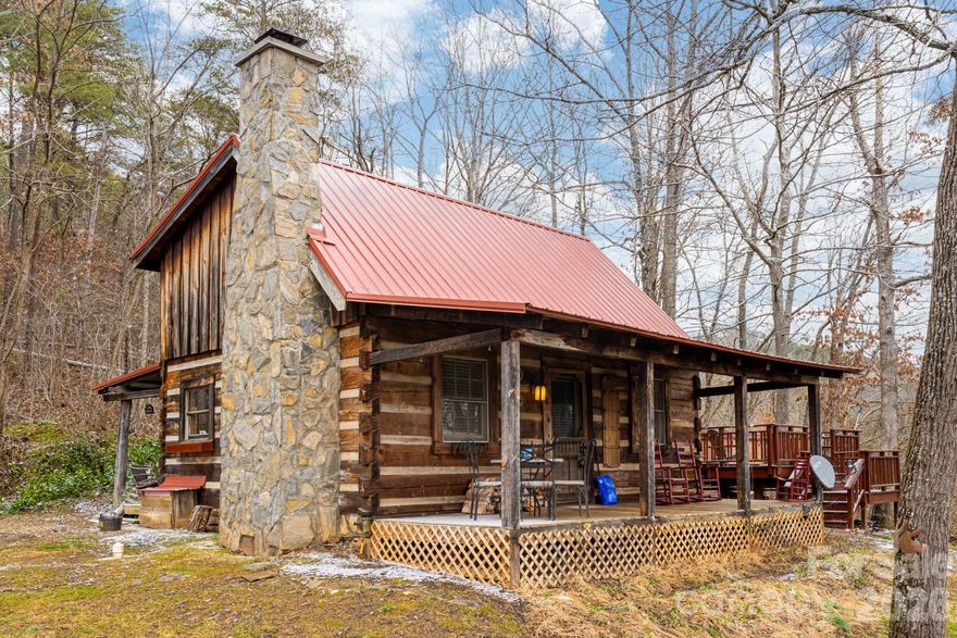Hand-Hewn Craftsmanship. River Views. A True Mountain Escape. Tucked away on 1.75 private acres overlooking the French Broad River, this hand-hewn log cabin offers a rare sense of place where craftsmanship, setting, and experience come together effortlessly. From the moment you arrive, there is a quiet magic to the property, inviting you to slow down and settle in.
Mornings begin on the rocking chair front porch, coffee in hand, as the soft sound of the river carries through the trees. Evenings are spent beside the striking wood-burning stone fireplace, its scale and texture anchoring the home’s warm, inviting interior. Vaulted ceilings and natural wood finishes create an open yet intimate atmosphere, with light filtering in to highlight the character of every beam and detail.
Designed for both relaxation and connection to the outdoors, the home offers multiple spaces to unwind, from the covered porch to the private deck with hot tub, where you can soak under the stars after a day of hiking, exploring, or simply enjoying the surrounding woods. Currently operating as a successful short-term rental, the property presents a compelling opportunity for continued income generation, while equally suited as a personal getaway or full-time residence. Whether you’re drawn by the craftsmanship, the setting, or the lifestyle it affords, this is more than a cabin, it’s an experience of Western North Carolina at its most timeless.