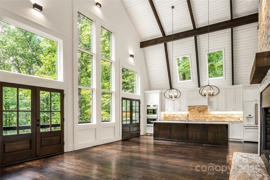 Welcome to your picture-perfect mountain oasis—an extraordinary residence that has undergone a down-to-the-studs luxury renovation, where every detail has been thoughtfully reimagined to the highest standard. Tucked among the trees offering a rare blend of refined design, modern comfort & serene, treehouse-like privacy just minutes from the heart of Burnsville. A dramatic open living space showcases a 300+ sqft expansion, soaring 30-ft ceilings & walls of windows that flood the home w/natural light & lush treehouse-like views from every vantage point. An open, flowing layout is anchored by the finest finishes throughout, creating an atmosphere that is both grand & inviting. At the heart of the home is a bespoke entertainer’s kitchen featuring extensive custom cabinetry & an oversized island that easily seats 6+. Premium matte white GE Café appliances include electric induction cooktop w/pot filler, French-door refrigerator, apron-front sink, double ovens, microwave drawer, dishwasher, disposal & striking custom pendant lighting—an ideal setting for both everyday living & elevated entertaining. Kitchen opens seamlessly into the sprawling GR, highlighted by a new wood-burning FP w/an impressive 18-ft stacked-stone surround, expansive firebox, rustic mantel w/artisan-crafted iron brackets & granite raised hearth. Fully appointed wet bar enhances the space w/custom cabinetry (including glass-front uppers), granite countertops, premium hardware, undermount stainless sink & dual wine refrigerators. Adjacent to the GR, newly added den/dining/seating rm features vaulted ceiling & 2nd FP w/shiplap surround, rustic mantel, iron brackets & granite hearth—perfect for intimate gatherings or relaxed evenings by the fire. 2 primary ensuite BRs, one on main level (fully wheelchair accessible) & one on upper level, each featuring elegant electric FPs w/shiplap surrounds & rustic mantels. 2 additional spacious guest BRs located on LL. 3.5 spa-inspired BAs boast custom marble & ceramic tilework, w/heated floors in 2 BAs. Both primary suites include large closets w/custom organizer systems & luxurious BAs w/double vanities & glass-enclosed tiled showers; main-level primary also features a bubble-jet soaking tub. Adding to the home’s versatility are 2 loft spaces. 2nd-level loft, just outside the upper primary suite, includes a granite-topped dry bar w/beverage/wine refrigerator, lighted glass shelving & lounge area. 3rd-floor loft—accessed by a tuck-away ladder—offers exceptional flex space for sleeping, office, or creative retreat, complete w/operational skylights, new windows & wall sconces. Thoughtful up-lighting along ceiling beams gently washes ceilings, creating a warm & inviting evening ambiance throughout. LL features 2 Guest BRs, a beautifully designed shared BA w/heated floors, glass shower enclosure, dual ceiling-mounted rain shower heads, handheld wands, new transom window & double vanity. LL includes multiple storage closets, wine rm w/custom wall-wash lighting (easily convertible to a media rm, home gym, or workshop), utility closet w/water filtration & softening systems & an attached garage. Multiple access points lead to a covered patio w/FP, including direct access from one of the BRs. Outdoor living is equally impressive w/a brand-new firepit & grilling area, exterior driveway & peaceful, private setting ideal for entertaining or unwinding beneath the stars. Additional highlights include new interior & exterior paint, new roof, new gutters w/gutter guards, extensive electrical & plumbing updates, new hybrid hot water tank, newer HVAC, new well & pressure pumps & fully serviced septic system (4-BR permit on file). Ideally located just 5 minutes from downtown Burnsville & Toe River Arts & only 35 minutes from Asheville, this exceptional property offers luxury, privacy & convenience—with no HOA fees & no hurricane damage. A truly remarkable mountain retreat where craftsmanship, comfort & setting come together in perfect harmony.