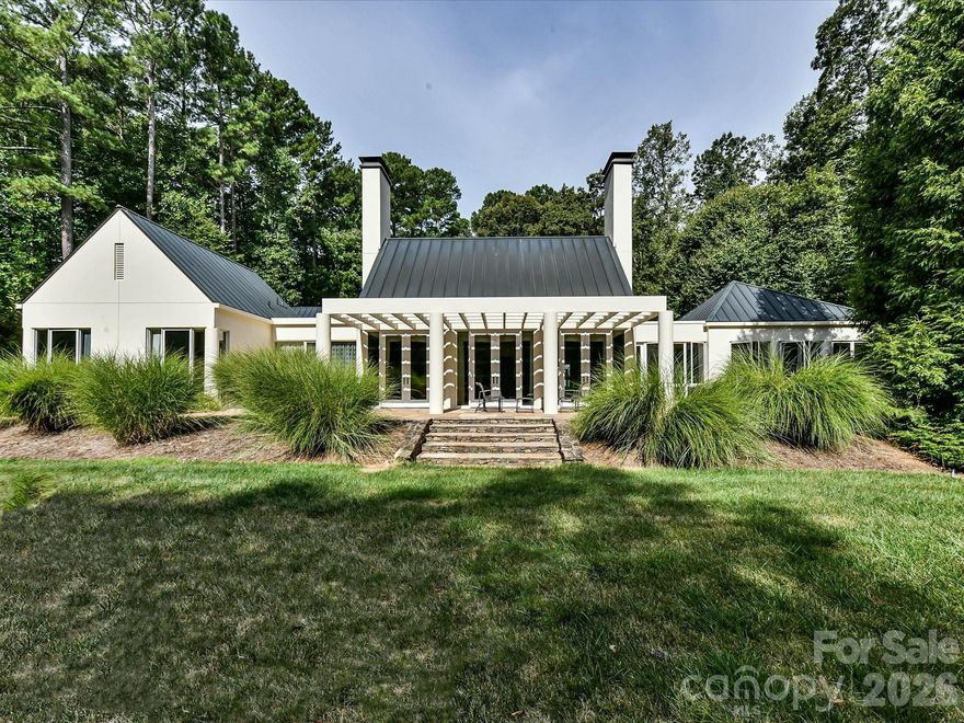 Located just 1.5 miles from downtown Davidson, 606 Ardrey Circle is one of the area’s most beautiful homes! The owners took great care in planning every single detail and have lovingly maintained it. The exquisite residence sits on a private 2.64-acre property, enveloped by gorgeous, mature trees. Accessory Dwelling Unit would most likely be allowed. Please confirm with the Town of Davidson. The grounds are absolutely beautiful, with a grassy lawn, stone walls and steps, woodland paths, stone firepit, sculptures and multiple spaces to relax. One of the most stunning features is a large stone waterfall that is visible from inside the house. There is ample room for a large pool and pool house. Built by Gene Keener (Fine Homes), the modern home was designed by Charlotte architect Jim Meyer and blends in perfectly with the natural surroundings.  Light is abundant in each room and outdoor spaces abound. Most of the living space is on the main level, including 4 bedrooms and  4 & 1/2 bathrooms. The oversized, custom glass front door is surrounded by transoms and leads to a gracious entrance hall and spectacular central gallery atrium with glass ceiling. The house is composed of six pods around the central living space. The spacious living room/ dining room is vaulted and features 2 wood burning fireplaces and a wall of French doors that open to a generous stone veranda with pergola with a lovely trellis ceiling. A partially covered tile patio off the great room offers an amazing view of the waterfall and the surrounding forest.  The great room has a wood burning fireplace and built-in bookcases and is open to the kitchen, which has honed granite counters and stainless steel appliances, including a gas stove and stainless steel vent.  A large butler’s panty for additional storage and counter space is adjacent to the kitchen. Ten foot ceilings downstairs, tall wood doors and built-ins add to the comfortable, elegant feel. The stone flooring in kitchen, family room and all 3 full baths is heated. The two primary bedrooms are located near the great room and back hall which leads to an oversized 2 car garage. A spacious laundry utility room is conveniently located there along with back stairs that lead to a bonus room and loft area. Two additional bedrooms with en-suite bathrooms are off the foyer.  There are two wells on the property that provide water for the waterfall feature & irrigation for the gorgeous grounds. 606 Ardrey Circle is an amazing home in a truly phenomenal location in the heart of Davidson.