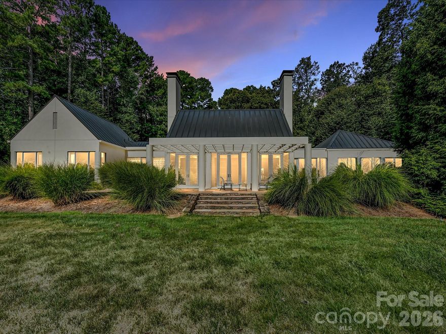 Located just 1.5 miles from downtown Davidson, 606 Ardrey Circle is one of the area’s most beautiful homes! The owners took great care in planning every single detail and have lovingly maintained it. The exquisite residence sits on a private 2.64-acre property, enveloped by gorgeous, mature trees. Accessory Dwelling Unit would most likely be allowed. Please confirm with the Town of Davidson. The grounds are absolutely beautiful, with a grassy lawn, stone walls and steps, woodland paths, stone firepit, sculptures and multiple spaces to relax. One of the most stunning features is a large stone waterfall that is visible from inside the house. There is ample room for a large pool and pool house. Built by Gene Keener (Fine Homes), the modern home was designed by Charlotte architect Jim Meyer and blends in perfectly with the natural surroundings.  Light is abundant in each room and outdoor spaces abound. Most of the living space is on the main level, including 4 bedrooms and  4 & 1/2 bathrooms. The oversized, custom glass front door is surrounded by transoms and leads to a gracious entrance hall and spectacular central gallery atrium with glass ceiling. The house is composed of six pods around the central living space. The spacious living room/ dining room is vaulted and features 2 wood burning fireplaces and a wall of French doors that open to a generous stone veranda with pergola with a lovely trellis ceiling. A partially covered tile patio off the great room offers an amazing view of the waterfall and the surrounding forest.  The great room has a wood burning fireplace and built-in bookcases and is open to the kitchen, which has honed granite counters and stainless steel appliances, including a gas stove and stainless steel vent.  A large butler’s panty for additional storage and counter space is adjacent to the kitchen. Ten foot ceilings downstairs, tall wood doors and built-ins add to the comfortable, elegant feel. The stone flooring in kitchen, family room and all 3 full baths is heated. The two primary bedrooms are located near the great room and back hall which leads to an oversized 2 car garage. A spacious laundry utility room is conveniently located there along with back stairs that lead to a bonus room and loft area. Two additional bedrooms with en-suite bathrooms are off the foyer.  There are two wells on the property that provide water for the waterfall feature & irrigation for the gorgeous grounds. 606 Ardrey Circle is an amazing home in a truly phenomenal location in the heart of Davidson.
