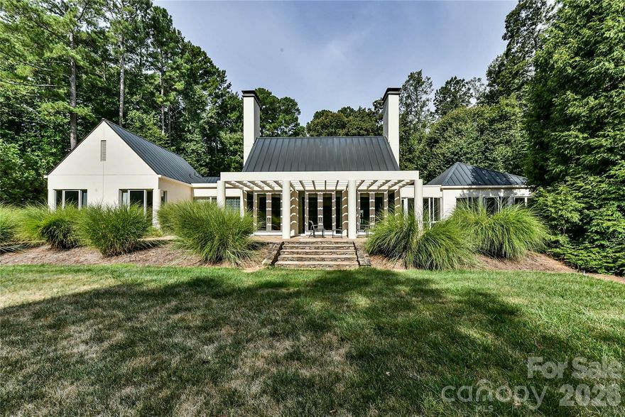 Located just 1.5 miles from downtown Davidson, 606 Ardrey Circle is one of the area’s most beautiful homes! The owners took great care in planning every single detail and have lovingly maintained it. The exquisite residence sits on a private 2.64-acre property, enveloped by gorgeous, mature trees. Accessory Dwelling Unit would most likely be allowed. Please confirm with the Town of Davidson. The grounds are absolutely beautiful, with a grassy lawn, stone walls and steps, woodland paths, stone firepit, sculptures and multiple spaces to relax. One of the most stunning features is a large stone waterfall that is visible from inside the house. There is ample room for a large pool and pool house. Built by Gene Keener (Fine Homes), the modern home was designed by Charlotte architect Jim Meyer and blends in perfectly with the natural surroundings.  Light is abundant in each room and outdoor spaces abound. Most of the living space is on the main level, including 4 bedrooms and  4 & 1/2 bathrooms. The oversized, custom glass front door is surrounded by transoms and leads to a gracious entrance hall and spectacular central gallery atrium with glass ceiling. The house is composed of six pods around the central living space. The spacious living room/ dining room is vaulted and features 2 wood burning fireplaces and a wall of French doors that open to a generous stone veranda with pergola with a lovely trellis ceiling. A partially covered tile patio off the great room offers an amazing view of the waterfall and the surrounding forest.  The great room has a wood burning fireplace and built-in bookcases and is open to the kitchen, which has honed granite counters and stainless steel appliances, including a gas stove and stainless steel vent.  A large butler’s panty for additional storage and counter space is adjacent to the kitchen. Ten foot ceilings downstairs, tall wood doors and built-ins add to the comfortable, elegant feel. The stone flooring in kitchen, family room and all 3 full baths is heated. The two primary bedrooms are located near the great room and back hall which leads to an oversized 2 car garage. A spacious laundry utility room is conveniently located there along with back stairs that lead to a bonus room and loft area. Two additional bedrooms with en-suite bathrooms are off the foyer.  There are two wells on the property that provide water for the waterfall feature & irrigation for the gorgeous grounds. 606 Ardrey Circle is an amazing home in a truly phenomenal location in the heart of Davidson.