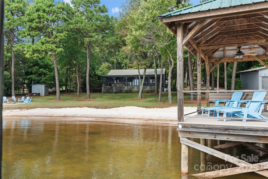 Experience serene sunsets and beautiful water views in this extensively renovated lake house, designed for relaxation and enjoyment. Nestled on a private lot, this home boasts 157 feet of shoreline with a beach and features an open floor plan with vaulted ceilings that create a spacious, airy feel. Enjoy mornings on the rocking chair back porch or unwind by the cozy fireplace in the living room. The backyard is perfect for gatherings, complete with a fire pit and a hot tub that overlooks the lake. For the boating enthusiast, the property includes a covered dock with a boat lift, a boat house, and a convenient boat ramp. Additional features include a seawall and an irrigation system to keep your landscape lush. Located off of Brawley School Rd just past Trump International Golf Club. Don't miss this opportunity to own a slice of lakeside paradise! NO HOA! Perfect vacation rental opportunity. Waterfront watersports boating dock enthusiasts dream!