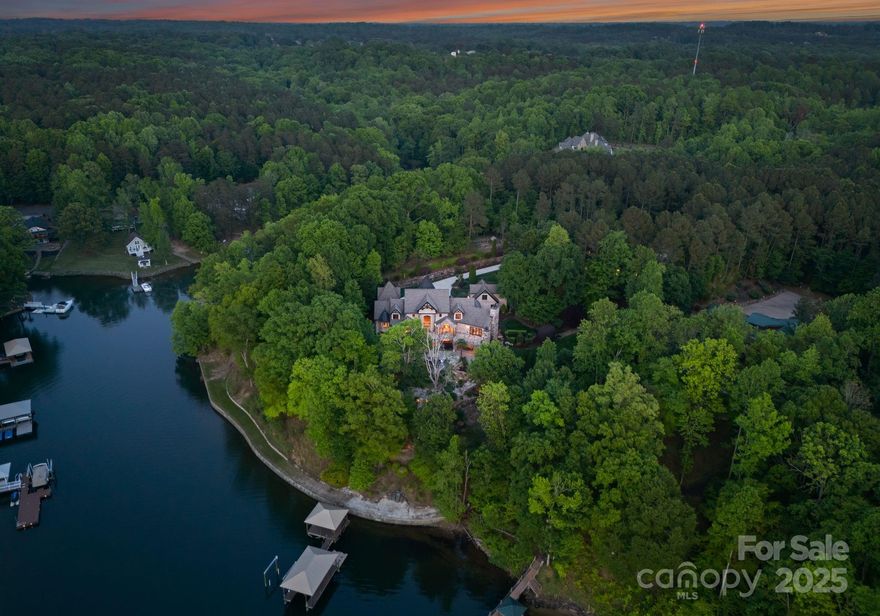 Home to NASCAR champion Martin Truex Jr., this private European-style estate on Lake Norman offers over 14,000 sq ft of luxury living on almost 5 gated, waterfront acres. A tree-lined drive leads to a stunning main house, carriage house with guest apartment, and expansive workshop/garage. The main home features a grand living room with soaring ceilings and lake views, a chef’s kitchen, formal dining, and a main-level primary suite with a spa bath and 2-story closet. Upstairs offers en-suite guest rooms and a second office with a loft. The finished basement includes a custom bar, theater, gym, and game area. Outside, enjoy a resort-style infinity pool, waterfall, fire pit, and private dock with boat lift. A detached garage with finished space above adds even more flexibility. This home is perfect for a car enthusiast, with ample amount of garage spaces and workshop. An entertainer’s dream and rare waterfront offering—experience luxury lake living with a championship pedigree.