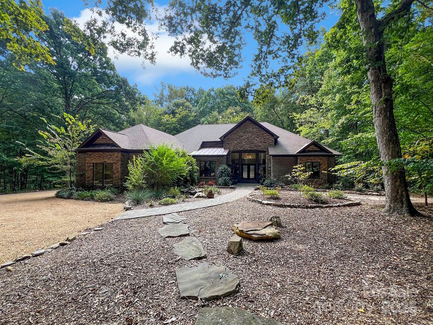 Welcome to Whispering Oaks blending rustic elegance with modern comfort in a private wooded setting. This 4-bedroom, 4-bath home welcomes with a circular drive, brick and stone accents, and lush landscaping with waterfalls and koi pond. Inside, walls of Jeld-Wen windows frame serene views, while features include travertine flooring, soaring ceilings, and three fireplaces. The chef’s kitchen boasts granite countertops, an American Range stove, and butler’s pantry, opening to dining and family areas. Outdoor living shines with a screened porch featuring a fireplace and motorized shades, plus multiple covered porches and patios. The luxurious primary wing offers dual closets, spa bath, and porch access. A versatile walk-out lower level includes additional bedrooms, second kitchen, and storage. Detached workshop, tankless water heater, and whole-home filtration add convenience. Located near top schools, shopping, and highways with low HOA, this estate is a rare retreat combining nature, craftsmanship, and refined living.