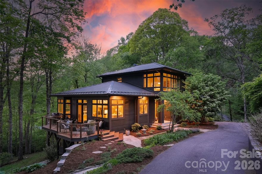 Tucked into over two private acres in the coveted Elk Mountain corridor, this custom residence is a rare convergence of intentional design, natural beauty, and elevated living. Fully reimagined by an interior designer, every element has been thoughtfully curated—layering handmade tile, natural stone, and bespoke finishes into a home that feels both grounded and refined. Thoughtfully designed, the home is positioned perfectly to capture the long-range sunset views from multiple vantage points - including the living room, kitchen, dining, primary suite and all 3 outdoor living spaces.

The main level unfolds with an effortless flow between living, dining, and a chef’s kitchen anchored by a Wolf range, Sub-Zero refrigeration, and striking quartzite surfaces. A guest suite or secondary primary just off the foyer, along with a walk-in pantry and laundry, offers true main-level living without compromise.

Upstairs, a dedicated primary retreat feels like a sanctuary—complete with dual walk-in closets and a spa-inspired bath designed for restoration. The lower level extends the experience with two additional bedrooms, a custom theater, wet bar, and a fully realized wellness suite featuring a sauna and cold plunge. 

Expansive Ipe hardwood decking spans all three levels, inviting year-round connection to the landscape. Designed by a landscape architect, the grounds are a living tapestry of native plantings, perennials, and edible herbs—recognized as a certified pollinator habitat, butterfly garden, and wildlife sanctuary. A gentle creek winds through the property, while long-range views, filtered morning light, and unforgettable sunsets create a dynamic natural backdrop.

Additional features include an elevator servicing all three levels, a standing seam metal roof, and a whole-house generator supported by a buried 1,000-gallon propane tank—capable of sustaining the home for extended periods.

Located just moments from the Blue Ridge Parkway and less than 15 minutes to downtown Asheville, this property offers the rare balance of seclusion and accessibility. With access to miles of neighborhood trails and preserved green space, 15 Hunters Way is more than a home—it’s an experience, intentionally crafted.