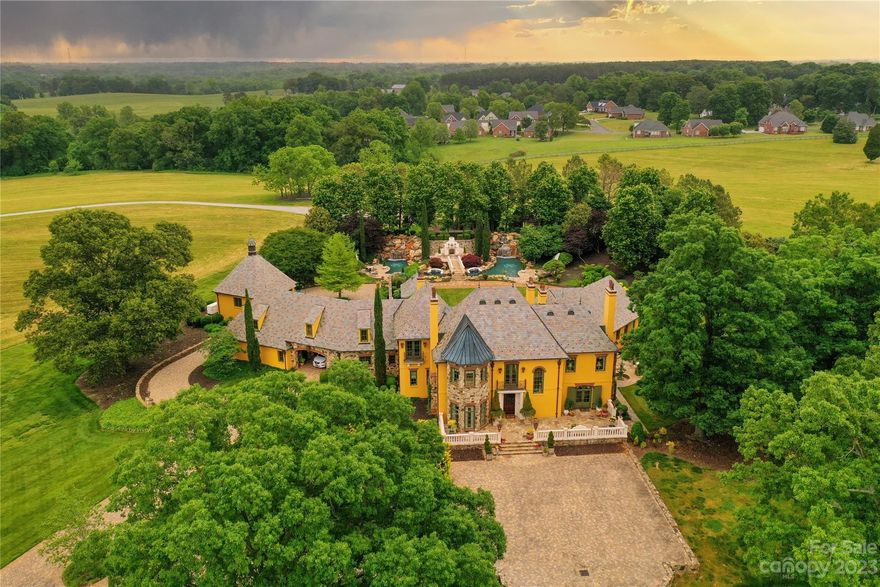 A French Country Estate nestled inside almost fifty sprawling fenced acres of rolling countryside at the edge of the mountains in Western N.C. Special finds throughout Europe were transported to this estate home to create a captivating manor house. Each artistic and architectural element has been thoughtfully & lovingly curated.  The home features a slate roof w/copper guttering & copper outdoor gas lanterns. Hand-painted murals & fleur-de-lis images appear on ceilings & walls throughout the manor’s spacious interior. Furnishings & textiles were custom & specifically crafted & curated. Antique stone floors, a custom-designed dual-fuel La Cornue range that is majestically placed inside a limestone niche with a custom-designed copper hood & flanked by handmade tiles are just a few of this home’s special features. Two soothing multi-tiered waterfalls flank each side of the luscious pool, a brand new outdoor fireplace, & adjacent patios, providing an impeccable private outdoor space.