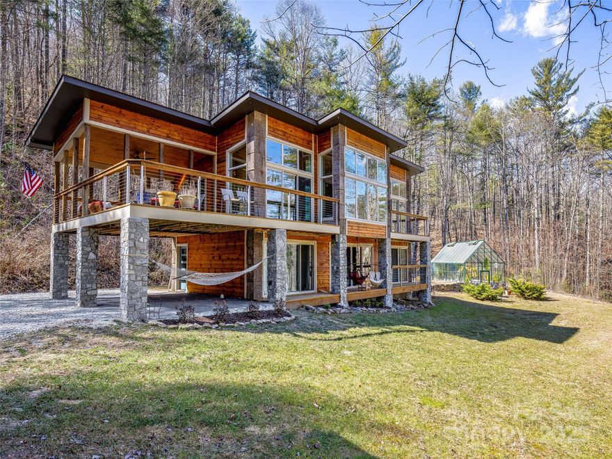 Nestled on 20+ acres of pure mountain beauty, this contemporary retreat embraces the outdoors with decks off every room, a large covered porch, and a private trail system.  Enjoy a peaceful pond and waterfalls. Just minutes from DuPont and Pisgah National Forests, adventure is always close by. Inside, the great room stuns with gas fireplace, walls of windows and well appointed kitchen. The lower level offers two bedrooms, a bath, laundry, and a cozy family room. A detached studio with a Peloton, row machine, sauna, and a two-car garage add to the practicality. The greenhouse that is humidity controlled is something special. 
After a mountain bike ride, rinse off in the outdoor shower or unwind by the fire-pit—your perfect mountain escape awaits!