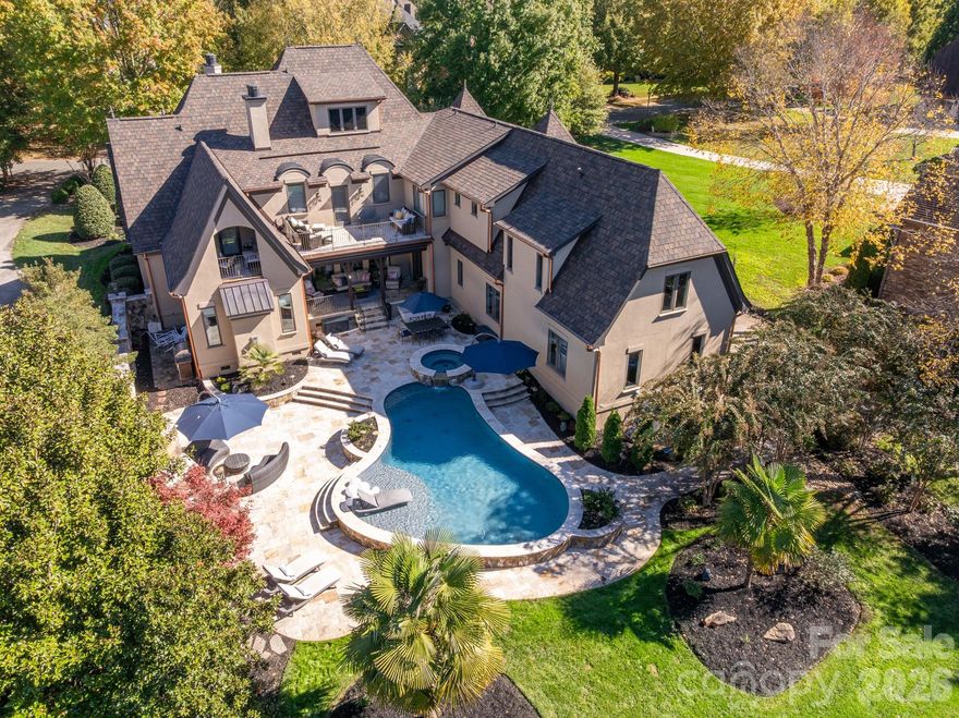 Luxurious 7,600+ sq ft home situated on a premium one-acre lot with water views, featuring resort-style amenities and located in the popular gated Chatelaine community of Weddington. So many great improvements, including a brand-new 50-year shingle roof with copper gutters, all-new HVAC system (2025), newly encapsulated crawlspace, newer water heaters, and so much more.
The beautiful interior includes custom high-end lighting throughout, luxurious millwork, gorgeous ceiling details, and generously sized spaces. The main floor features a stunning formal room with rich mahogany wall paneling and fireplace, plus an oversized Great Room with a carved limestone fireplace and dramatic coffered ceiling.
The luxury kitchen features stainless steel appliances, including a 6-burner commercial gas range with griddle, commercial hood, double ovens, a large counter-height island with seating, double sinks, high-end cabinetry with crown moulding, a fully equipped wet bar with beverage refrigerator and overhead illuminated glass storage, and a walk-in pantry.
Also on the main floor is the primary “wing,” aptly named for its impressive footprint, featuring a spacious bedroom, large sitting area with private access to the back terrace and pool area, two walk-in closets, and a luxury tile bathroom with separate vanities.
The second level is just as impressive, featuring three oversized secondary ensuite bedrooms, each with a walk-in closet, plus a large secondary retreat ideal as a second primary bedroom or expansive guest suite. Also on this level is an oversized bonus/fitness room with access from the rear staircase and a 350-square-foot loft that opens to a second-level terrace overlooking the resort-style backyard.
The third level offers even more living space with a dedicated theater room, a large recreation room with built-in wet bar, and a half bath.
No detail was spared on the exterior. Manicured landscaping enhances the front and back yards, with elegant paver walkways throughout. A private resort-style outdoor living area includes a saltwater pool with hot tub, outdoor sitting area with wood-burning fireplace, expansive travertine decking, and a covered porch. The property also features an expansive yard and beautiful water views. Zoned for top-rated Weddington schools.