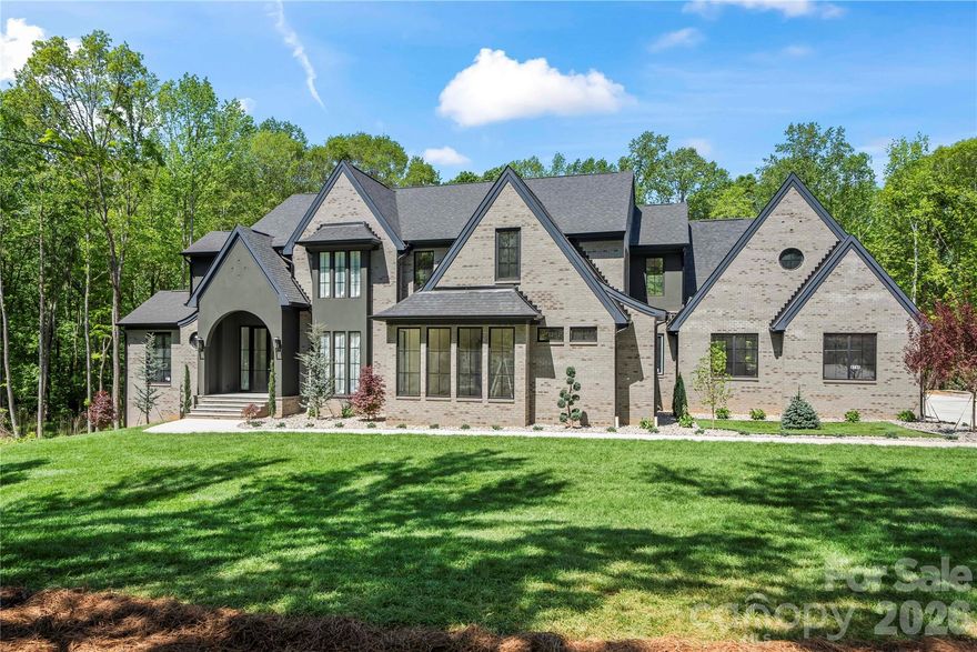 Stunning custom-built Modern European estate blending timeless architecture with refined luxury on a private wooded setting in Indian Land. This exceptional four bedroom, six bath residence showcases dramatic rooflines, designer finishes, and thoughtfully curated spaces throughout.
The open-concept floor plan features wide-plank engineered floors, soaring ceilings, abundant natural light, and seamless indoor-outdoor living. The gourmet chef’s kitchen is equipped with custom cabinetry, built-in Wolf and Sub-Zero appliances, premium countertops, and an oversized entertaining island. A separate butler’s pantry with additional appliances provides both convenience and elevated functionality. The quiet, secluded primary suite located on main level  offers panoramic views, an extra-large shower, a freestanding tub, and two massive walk-in closets. Laundry rooms on both levels for convenience. Designed for entertaining, this home also features a private wine cellar, a dedicated coffee room with a wet bar and an extra-large bonus room that can easily be converted into a theater. The exterior offers striking curb appeal with dark brick, steep gabled rooflines, and professional landscaping, creating a true luxury retreat.The encapsulated crawl space (with dehumidifier) helps prevent water intrusion, reducing the risk of mold and structural damage while improving energy efficiency. This gorgeous home is located just minutes from Ballantyne’s shopping, dining, parks, and entertainment. Don’t miss this rare opportunity to own a brand-new home with architectural charm, surrounded by trees that provide exceptional privacy — all with no HOA.