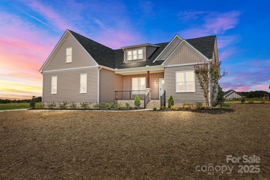 Impressive new construction with main-level living plus a spacious upstairs bonus room. This home sits on a wide country lot in Locust and offers both comfort and style. The main level features an open living, dining, and kitchen area with white shaker cabinetry, granite countertops, a mosaic tile backsplash, stainless steel appliances, and pendant lighting—perfect for everyday living and entertaining.

The primary suite includes a coffered ceiling, a large custom walk-in closet, and a spa-inspired bathroom with dual vanities, an oversized tiled shower with a built-in bench, and a glass enclosure. Two additional bedrooms and a beautifully finished full bathroom complete the main floor.

Upstairs you will find a massive bonus or flex room along with a full bathroom, providing the ideal space for a playroom, media room, guest suite, or home office. A large walk-in attic makes storage easy and convenient.

Outdoor living shines with a welcoming front porch and a covered back patio with a ceiling fan overlooking open green views. A long concrete driveway leads to the attached two-car garage, and a storage building sits nearby for added convenience.