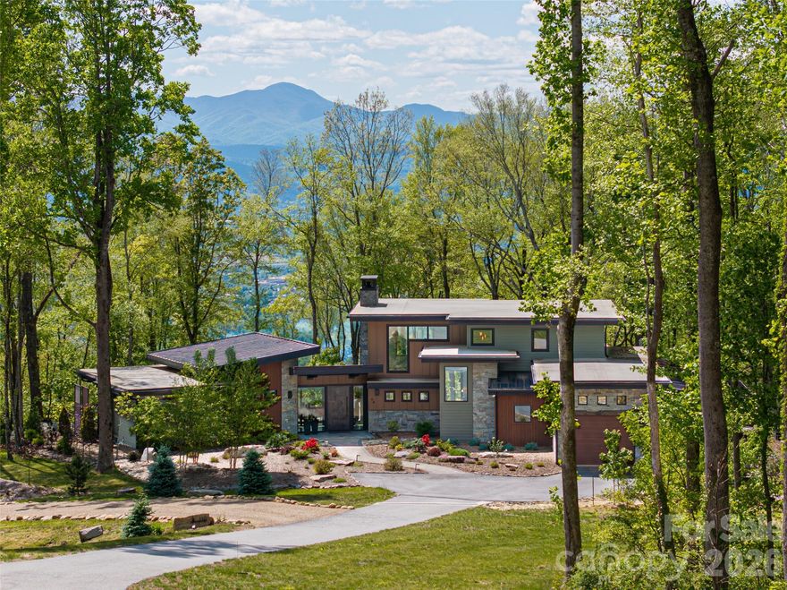 Embrace refined mountain living in this striking contemporary estate, where serenity and sophistication converge atop a rare flat mountaintop setting in the gated conservation community of Couch Mountain. Sweeping 180-degree Blue Ridge Mountain views unfold through expansive walls of glass, creating a breathtaking backdrop from nearly every room while timeless craftsmanship and elevated design define the living experience.

This exceptional property is being offered three separate ways to suit a variety of lifestyles and investment opportunities: this listing includes the residence and the lot it is on plus the adjoining lot; the home is also available with only the individual lot; or the additional homesite may be purchased separately. Together, the offerings present a rare opportunity to secure privacy, flexibility, and long-term value in one of Western North Carolina’s most distinctive mountain communities.

Inside, the dramatic great room showcases soaring 20-foot ceilings, hand-hewn 125-year-old beams reclaimed from a Canadian barn, exposed custom steel supports, and a stunning stacked-stone fireplace anchored by a concrete hearth. Designed for both grand entertaining and comfortable everyday living, the open-concept floor plan flows effortlessly into the gourmet kitchen, where Thermador stainless steel appliances, Italian quartzite countertops, and bespoke rustic alder cabinetry create a space that is as functional as it is beautiful. A walk-in pantry and coffee bar, concealed behind a sliding knotty alder barn door, add warmth and character.

The adjoining dining area and sunroom—with its inviting stone fireplace and panoramic mountain vistas—offer seamless indoor-outdoor living and memorable gathering spaces year-round. The main-level primary suite is a luxurious retreat featuring breathtaking views, a spa-inspired oversized shower, and a custom walk-in closet thoughtfully designed for comfort and organization. Upstairs, two private ensuite guest bedrooms showcase artisanal tilework and refined finishes, providing elevated accommodations for family and visitors alike.

Outdoors, the curated mountain landscape invite exploration and relaxation with established gardens, walking trails, natural stone features, and a fenced vegetable garden. Whether enjoying sunrise coffee on the terrace, entertaining beneath the stars, or simply taking in the stillness of the mountains, the setting is both peaceful and inspiring.

Ideally located just 15 minutes from Asheville Regional Airport and conveniently positioned between Asheville and Hendersonville, the property offers easy access to acclaimed restaurants, shopping, arts, and outdoor recreation. Community-approved seven-day rentals also create the opportunity for a lock-and-leave lifestyle with potential income-producing flexibility when not in residence. Rarely does a property combine architectural distinction, panoramic views, privacy, and versatility so seamlessly in one extraordinary mountain offering.