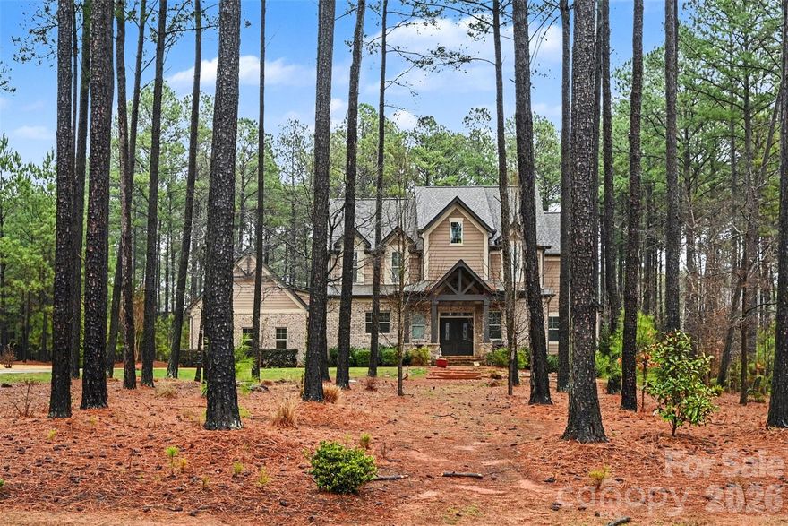 Tucked away on a beautifully private, wooded homesite in Riverchase, this custom brick home offers refined living with exceptional indoor and outdoor spaces designed for both relaxation and entertaining. Set on just under an acre, the property welcomes you with a stately façade, inviting front porch, and timeless architectural presence that blends seamlessly into its natural surroundings.

Inside, the open floorplan is filled with natural light and anchored by a warm, inviting living room with a gas log fireplace, creating the perfect gathering space. The kitchen features an oversized island, abundant cabinetry, and thoughtful built-in details, flowing effortlessly into the dining and breakfast areas for easy everyday living and entertaining. Rich wood flooring and quality finishes add to the home’s elevated feel.

The main-level primary suite is a true retreat, offering privacy and comfort with generous proportions, a spa-like bath, and spacious walk-in closet. Having the primary bedroom on the main floor provides both convenience and long-term livability. Upstairs, 2 additional bedrooms with private ensuites and a versatile family room create flexible space for guests, hobbies, or media.

Step outside to a thoughtfully designed courtyard setting that feels like your own private escape. The in-ground pool has already been installed and awaits the finishing touches from its next owner, offering the opportunity to complete a stunning outdoor oasis tailored to your vision. A patio and covered porch provide multiple areas to relax, dine, and entertain while enjoying the peaceful, wooded backdrop. Evenings can be spent gathered around the fire pit under the Carolina sky.

The detached garage includes a dedicated shop area currently set up as a home gym, offering incredible flexibility for fitness, hobbies, or creative pursuits. Located in the sought-after Riverchase community with access to resort-style amenities and scenic walking trails, this home combines privacy, space, and lifestyle in one exceptional Lancaster property