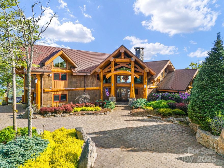 Perched on a pristine ridge with endless views of the Blue Ridge Mountains, this remarkable timber frame estate blends mountain elegance with timeless craftsmanship. From the moment you arrive, you're welcomed by hand-hewn beams, soaring ceilings, and panoramic vistas. A dramatic glass floor in the foyer offers a stunning view into the custom wine cellar below, setting the stage for the artistic details throughout. The great room features vaulted timber trusses and a striking Chihuly-style chandelier, while walls of glass invite the outdoors in. The primary suite offers a spa-like bath, walk-in closet, and private terrace access, perfect for soaking in the mountain views. In addition to the attached two-car garage, a detached garage includes a 2-bedroom, 2-bath guest apartment with full kitchen, living area, and private entrance—ideal for guests or upscale rental use. Whether hosting or enjoying peaceful mornings above the clouds, this property offers unmatched serenity and style.