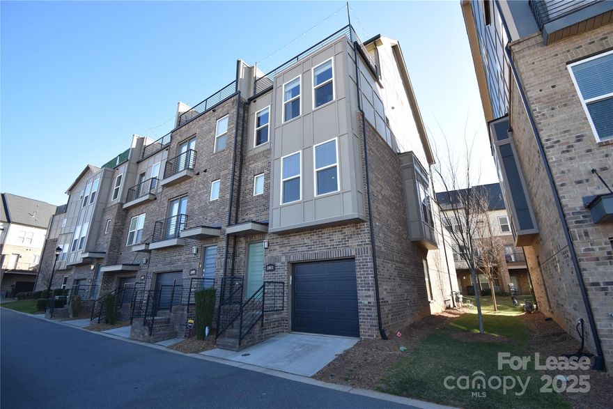 Located in the gated South Village community, this 2019-built end-unit townhome offers a modern take on LoSo living with space, privacy, and thoughtful upgrades throughout. The home features three bedrooms and three-and-a-half baths across multiple levels designed for flexibility and everyday comfort. On the main floor, hardwood flooring, an open-concept design, and added end-unit windows create a bright, welcoming atmosphere. The kitchen opens effortlessly into the dining and living areas, making it ideal for both daily living and entertaining, while upgraded wood stair treads add a refined touch.

Technology and lifestyle enhancements elevate the experience, including a wired surround-sound system with separate zone controls for indoor areas and outdoor balconies. The oversized two-car tandem garage includes an epoxy-coated floor, additional storage space, and direct access to a private lower-level patio. Upstairs, the third floor houses the bedroom level, while the fourth floor introduces a versatile flex space currently set up as a music studio, complete with sound-dampening foam panels and a solid, airtight door—perfect for creative work, remote office use, workouts, or hobbies that benefit from separation.

Just beyond this flex room, a private rooftop terrace offers expansive views and a relaxing outdoor retreat ideal for coffee at sunrise or hosting friends in the evening. Positioned in one of Charlotte’s most vibrant neighborhoods, this secure community places you minutes from breweries, dining, shopping, the RailTrail, light rail, and easy Uptown access.