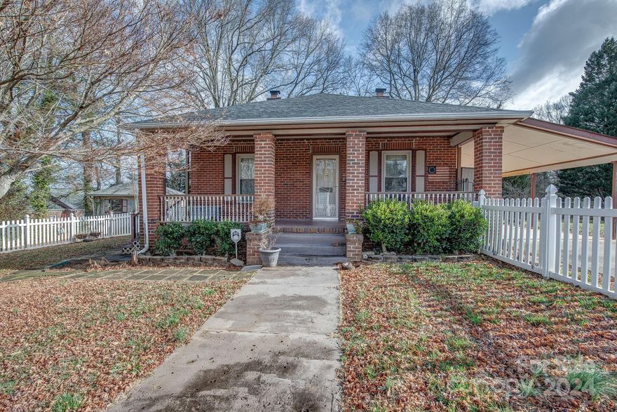 Nestled in Mount Holly, NC, this charming brick cottage exudes warmth and character. Beyond its white picket fence lies a welcoming rocking chair front porch, perfect for lazy afternoons. Inside, discover 2 bedrooms, 1 full bath, and a sunroom flooded with natural light. Built-ins adorn the dining room, adding to the home's appeal. Enjoy the convenience of a utility room with laundry. Step outside to a large, covered deck overlooking the landscaped yard, complete with an outbuilding for extra storage. Close to downtown and schools, this home offers the ideal blend of comfort and convenience.