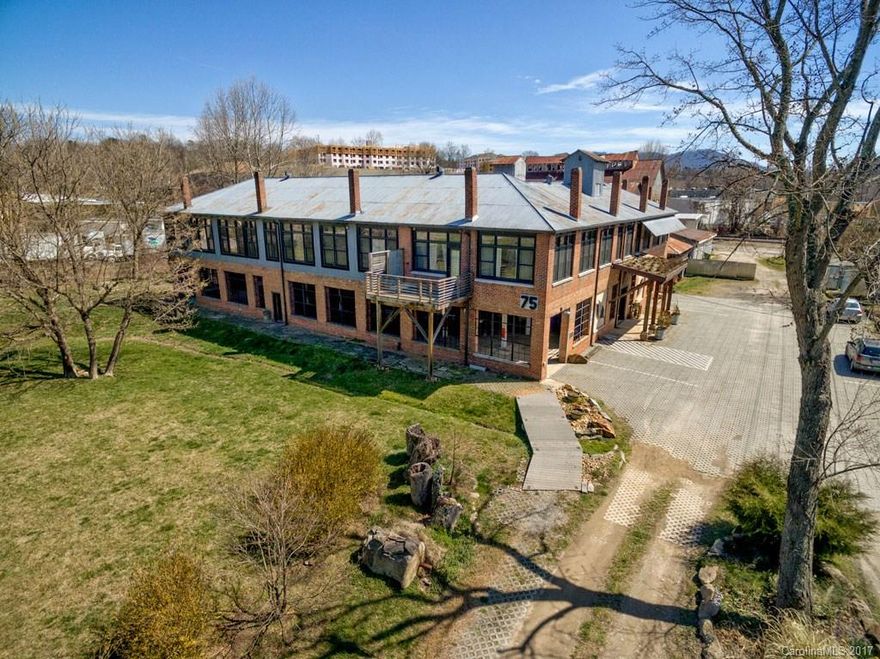 Modern Industrial condo in an Eco-Friendly community. Corner loft-style unit has original hardwood floors, 15 ft+ ceilings in living & dining room, exposed brick and ductwork, and huge windows. Modern open floor plan. Kitchen has breakfast bar, modern fixtures, and energy star appliances. Reclaimed wood stairs lead to loft bedroom. Enjoy the community spaces and front lawn. Designated covered parking space comes with unit. Walkable to all of Biltmore Village, Hillman Brewery and  Moe’s BBQ.