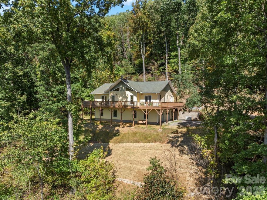 This stunning residence – a 3 BR/3BA/2.5 car garage with an additional DETACHED oversized 2-car garage and studio/accessory dwelling unit (ADU), bathroom, and stand-up attic – enjoys year-round mountain views of Cold Mountain and the Pisgah Forest beyond. This Western North Carolina sanctuary is thoughtfully designed for
privacy and low maintenance. The home is equipped with a Generac generator to provide continuous power for your peace of mind. Enjoy your morning coffee and sip wine at sunset from your favorite spot on the wrap-around open-air deck that provides breathtaking views of the sweeping vistas, peaks and valleys. A covered deck/porch greets and welcomes you before entering the home. Step inside the front door to be impressed by the natural beauty of the tongue-and-groove, white pine cathedral ceiling, and the great room gas log, stone fireplace, flanked by overhead windows and glass paned doors on either side that lead to the open-air deck and the amazing panoramic views beyond. A perfect place for entertaining and gathering, the open concept main
level allows ample space for interaction among friends and family. The kitchen is equipped with Corian countertops and beautifully crafted, custom shaker-style cabinets. The laundry/mud room and pantry area, adjacent to the kitchen, provides sought-after additional storage. The split-plan bedrooms boast ensuite bathrooms. The primary suite is a true sanctuary with elegant French doors leading to the bubbling hot tub that, again, captures the amazing mountain views. The primary ensuite includes a large walk-in closet as well as a spacious bathroom with a custom-tiled, walk-in shower and a beautiful claw-foot cast iron soaking tub. The main-level guest suite shares the same picturesque views. The terrace lower level provides additional living/flex space, an under-stair closet, a third bedroom, a separate bathroom, and access to the 2.5 car garage. The oversized, DETACHED, 2-car garage, studio/ADU and bath, with stand-up attic space above, allows additional living and storage space. The French doors of the studio lead to a private lawn – a true secluded oasis. The Generac generator, two leased propane tanks, a private well with pressure tank and water filtration system, ensures
your comfort throughout the year. Don’t miss this opportunity to enjoy your own private mountain paradise. Schedule your showing today!  Furnishings negotiable.  This property experienced NO DAMAGE during Hurricane Helene.