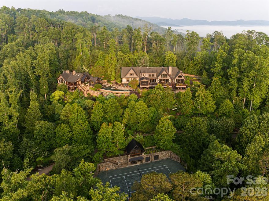 Just minutes from downtown Asheville, 66 North Deerhaven Lane is an extraordinary gated luxury estate in Asheville, N.C. offering over five acres of private gardens, award-winning landscape design and refined mountain living in the heart of the Blue Ridge Mountains. Known as Deerhaven Gardens, this remarkable property combines architectural elegance, world-class outdoor living and exceptional privacy just minutes from Asheville’s dining, arts and cultural amenities. The residences were completely renovated and expanded in 2011 with the estate’s grounds were masterfully designed by renowned Asheville landscape architect Charles Clay Mooney, whose work at Deerhaven Gardens earned the American Society of Landscape Architects’ highest national award. The property is centered around a spectacular 77-foot infinity-edge swimming pool with cascading waterfalls, natural stone terraces, streams and botanical gardens, recognized by Luxury Pools & Outdoor Living Magazine as Best Overall Outdoor Living Design in the United States. The main residence is designed to seamlessly blend indoor and outdoor living. A dramatic great room with vaulted ceilings, exposed beams and tongue-and-groove paneling opens through more than 200 feet of NanaWall accordion glass doors, creating an indoor-outdoor mountain retreat. Imported stone surfaces and natural materials complement the surrounding landscape while providing sophisticated luxury finishes throughout. At center of the home, the chef’s kitchen features a 60-inch Wolf range, Sub-Zero refrigeration, dual Miele dishwashers and custom cabinetry, opening to expansive living and dining spaces ideal for entertaining. Modern systems include fully integrated smart-home technology, geothermal HVAC, backup generators and advanced lighting, security and climate controls. The primary suite offers a private sanctuary with fireplace, spa-inspired bath, heated floors, steam shower, jetted soaking tub and custom cabinetry. Upstairs guest suites and an executive office capture sweeping sunrise views across the Blue Ridge Mountains. The terrace level recreation wing includes a media lounge, billiards room, full bar, wellness room, and fitness studio with direct access to the pool terrace and gardens. A separate guest house provides exceptional flexibility with its kitchen, living room, primary suite, bunk room and recreation space, ideal for hosting extended guests, multigenerational living or private staff accommodations. Outdoor amenities are equally impressive and include multiple entertaining terraces, a screened porch with hibachi grill, poolside summer kitchen and bar, and a private tennis court with observation deck and outdoor wet bar. Meandering paths wind through curated botanical gardens, tranquil ponds and wooded trails, creating one of the most remarkable private estates in the Southeastern United States. Despite its serene setting, the property is exceptionally convenient, approximately 15 minutes to downtown Asheville, eight minutes to Biltmore Forest Country Club, five minutes to the Blue Ridge Parkway, and under 15 minutes to Asheville Regional Airport and private aviation at Signature FBO. Offered turnkey with select exclusions, Deerhaven Gardens represents a rare opportunity to own one of Asheville’s celebrated luxury estates, combining privacy, architectural design, award-winning gardens and world-class outdoor living in the Blue Ridge Mountains.