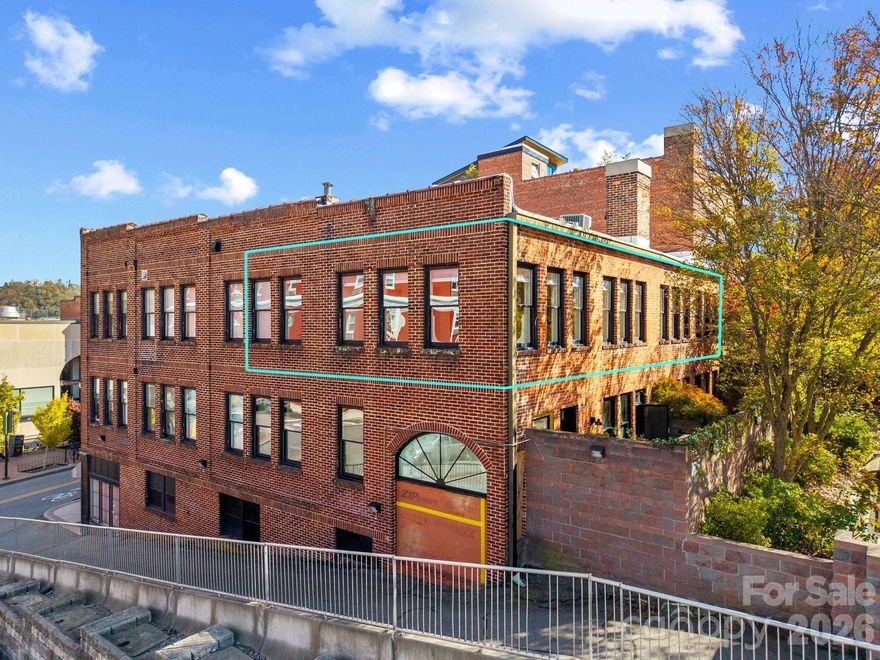 Exclusive Haywood Street Downtown Condo! Welcome to a rare, expansive, 1,939-SF single-level residence at 60 Haywood Street, created by combining two units into a 2 BR/2 BA home. As a top-floor corner unit, you’ll enjoy unparalleled quiet and privacy with no one above you. The spacious, open-concept living area features 9-foot ceilings, solid hickory floors, and 17 big windows offering incredible views of the Basilica of St Lawrence church and long-range mountain vistas. The kitchen is open and ready for your touch, complete with incredible countertop space and a deep, floor-to-ceiling pantry. Mirrored French doors separate the main living space from the private quarters. This secluded area encompasses two peaceful bedrooms, an office/sitting area, and an enormous walk-in closet—featuring custom built-ins and a dedicated laundry closet. Crucially, this home includes two permanent, designated parking spaces and four large, private storage units in the basement. One cannot beat this downtown location! Just steps from the Grove Arcade, Harrah’s Cherokee Center, shopping and fine dining, and housed in a historic 1928 building, this condo offers unique charm and modern convenience.