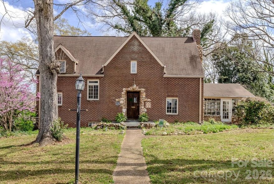 Step into a piece of Kings Mountain history at 210 N. Gaston Street, the original home of A.J. Mauney, built in 1932 and rich with timeless character and craftsmanship. This 3 bedroom, 2.5 bath historic brick home sits on a beautiful lot with mature trees and classic curb appeal. Inside, the home showcases the craftsmanship of the era with hardwood floors, rich wood trim, exposed beam ceilings, and original built-ins throughout. The main living room features a striking stone fireplace and custom built-in bookcases, creating a warm and inviting space full of historic charm.  A formal dining room offers an elegant setting for gatherings, while large windows throughout the home bring in natural light and highlight the home's architectural details.  One of the home's most unique spaces is the expansive sunroom surrounded by walls of windows, creating a bright and relaxing space ideal for entertaining, reading, or enjoying the surrounding views year-round.  In the basement you’ll find Mr. Mauney’s original darkroom, reflecting his passion for photography and adding another fascinating historical element to the property.  Original architectural details including solid wood doors, vintage hardware, built-ins, and detailed millwork help preserve the home's historic character while offering comfortable everyday living.  Located near the heart of Kings Mountain, this property provides convenient access to downtown shops, dining, parks, and local amenities while preserving the charm of one of the area's historic residences.  Seller is offering a $25,000 credit to the buyer to be applied toward upgrades or improvements, providing a great opportunity to personalize and enhance this historic property.