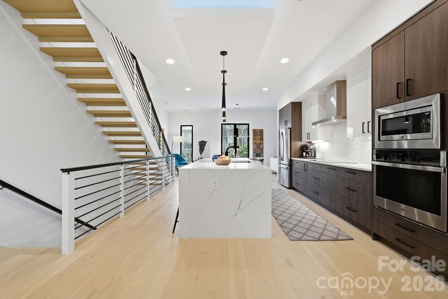 Discover LUX NoDa, an exclusive enclave of architecturally striking townhomes in the heart of Charlotte’s vibrant NoDa Arts District. Designed to impress, these residences blend modern sophistication with curated detail, from permeable driveways and bold façades to thoughtfully designed interiors.

The main level welcomes you with a dramatic floating staircase and spacious foyer. A private guest suite, currently styled as a flex office, features a wet bar with beverage fridge, full bath, and direct access to the backyard, offering ideal privacy for guests or work-from-home flexibility.

Upstairs, the primary living level is designed for entertaining. Ten-foot ceilings, oversized windows and abundant natural light highlight the home’s clean architectural lines. The open-concept living, dining, and kitchen spaces flow seamlessly, anchored by a showstopping chef’s kitchen. Culinary enthusiasts will appreciate the European cabinetry, waterfall quartz countertops, under-cabinet and ceiling accent lighting, gourmet sink with premium attachments, and high-end appliances including a 36-inch induction cooktop. A sleek linear electric fireplace creates an inviting atmosphere, while sliding doors open to a private balcony overlooking the manicured turf yard.

The top level hosts the primary retreat with vaulted ceilings, custom blinds,  custom walk-in closet system, and a private balcony nestled among the treetops. The spa-inspired bath features a luxurious walk-in shower, dual vanities, and a skylight that fills the space with natural light. An additional guest suite with private ensuite and dual closets completes this level.

Additional highlights include an oversized one-car garage with built-in storage and electric vehicle charger, custom exterior lighting, and a striking entrance sculpture that enhances the community’s artistic character.
Located just steps from NoDa’s eclectic dining, breweries, boutiques, entertainment, and light rail, with convenient access to Uptown, this home offers low HOA dues and an exceptional urban lifestyle. Experience modern elegance at LUX NoDa!