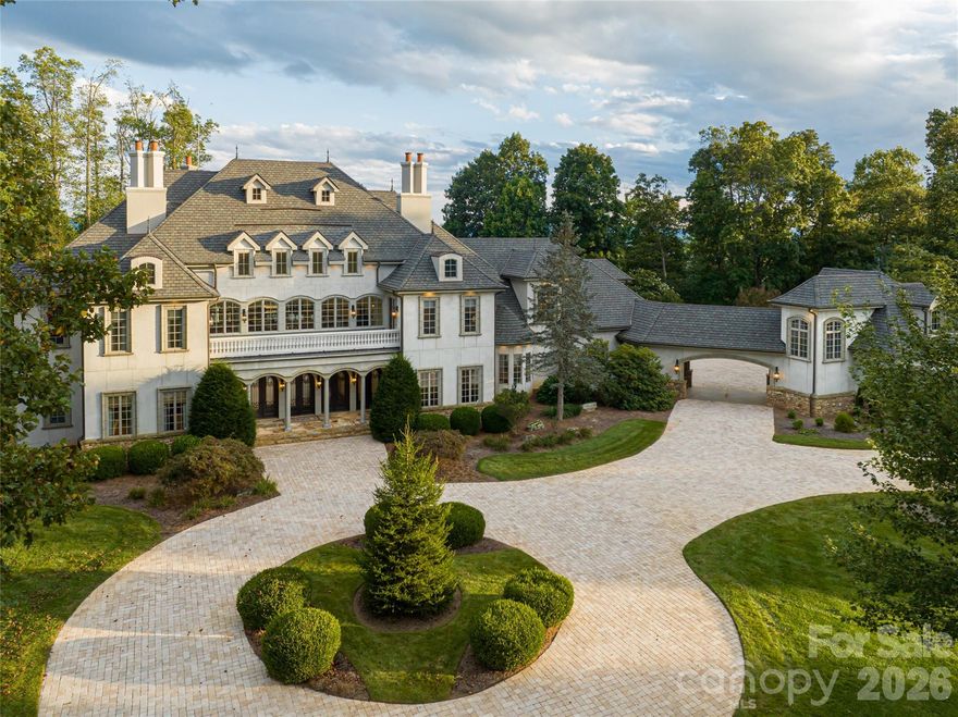Set atop a private ridge in Biltmore Park, this privately gated European-inspired estate spans 2.51 acres of level, professionally landscaped grounds with seasonal Blue Ridge Mountain views. Thoughtfully re-imagined by the owner, the home has been curated with a more transitional aesthetic that blends timeless architectural character with a lighter, more modern approach to luxury living. Within one of Asheville’s sought-after communities, the property offers exceptional privacy alongside prized walkability, community amenities and access to top-rated schools. The grand two-story foyer introduces refined interiors, anchored by a spiral staircase, floor-to-ceiling fireplace and expansive windows that maximize natural light. Designed for seamless indoor-outdoor living, the main gathering area opens to a private poolside retreat with a newly refinished swimming pool, spa, pool house, covered porch and hard-scaped entertaining areas. The main-level owner’s wing features newly installed black walnut hardwood floors, a sitting parlor with marble fireplace, and a spa-style bath complete with backlit Cristallo quartzite, whirlpool tub, heated floors, marble walk-in shower, dual vanities, dual closets and discreet in-suite laundry. The fully redesigned kitchen was created to serve as a functional gathering space and a refined focal point of the home. Custom cabinetry, new appliances, a tower wine refrigerator, statement range hood, and layered granite and quartzite surfaces create a sophisticated yet welcoming aesthetic. Seamlessly connected to the fireside keeping room and outdoor entertaining areas, the space was designed for effortless everyday living and hosting alike. The upper level includes four en-suite bedrooms, a bonus room and a second large laundry room. A cobblestone circular drive leads to a three-car attached garage and a detached two-car garage with an additional finished flex space above. Offering privacy and proximity, this residence is minutes from Biltmore Park Town Square, the Blue Ridge Parkway, Asheville Regional Airport and premier Asheville shopping and dining. For those seeking a luxury estate with mountain views and architectural distinction, this Biltmore Park residence delivers elegance, scale and lifestyle integration.