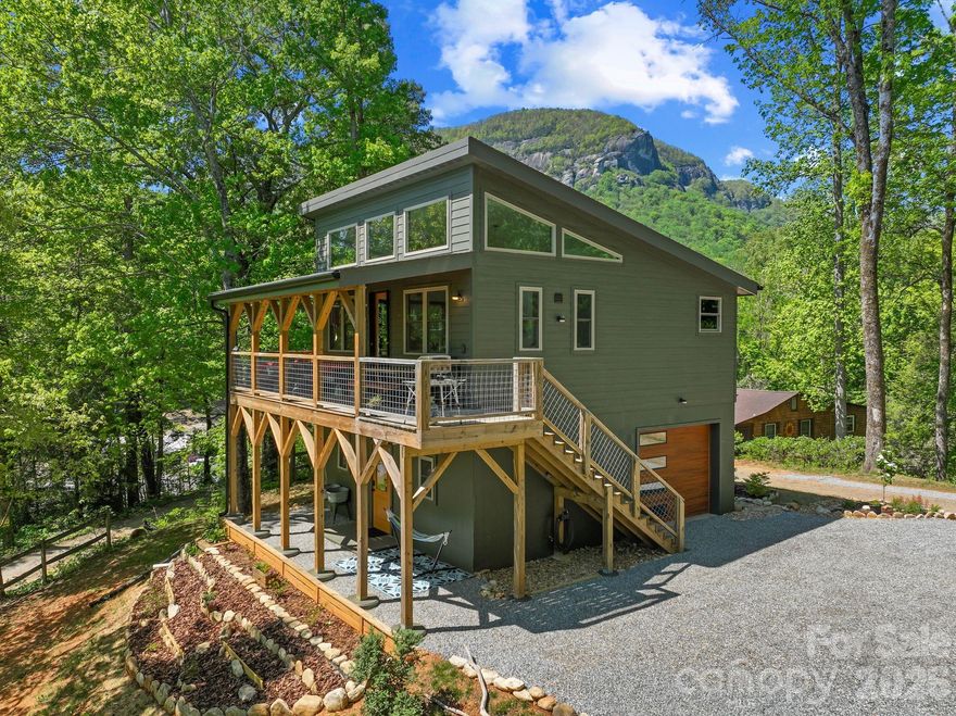 Lovingly known as “The Bird House,” this one-of-a-kind mountain modern retreat is perched within a lush tree canopy, offering a rare sense of privacy, elevation, and connection to nature. Designed to feel immersed in its surroundings, the home captures a unique perspective of the landscape, where seasonal glimpses of Lake Lure and iconic Chimney Rock emerge through the trees and shift beautifully throughout the year.

The main living level unfolds from a covered deck and is thoughtfully composed with soaring ceilings, expansive windows, and a seamless indoor-outdoor connection. The kitchen features quartz countertops, custom cabinetry, GE Café Series appliances, and tambour wood detailing carried through the island, vent hood, fireplace surround, and pantry door. The living space is anchored by a striking fireplace wall with geometric accents and a sleek linear electric fireplace, enhanced by curated lighting that creates a warm, gallery-like ambiance. A well-designed bedroom and full bath complete the main level, offering a comfortable and efficient primary living space.

The separate lower level, with private exterior access, provides a studio-style living area complete with a kitchenette — ideal for guests, extended stays, or flexible use. In addition, the attached heated and cooled garage offers valuable flex space, easily suited for a game room, fitness studio, or creative workspace.

Set on a total of 1.01 acres across two lots, the property offers additional space and flexibility, with potential for future use or expansion (buyer to verify). Built with intention, the lower level features 10-foot Superior concrete walls, paired with cement board siding above for durability and efficiency. With no HOA restrictions, the home lends itself equally well to a full-time residence, seasonal retreat, or potential rental opportunity. In addition to all of the above, the home also offers full RV hookup & an EV Charger!

Tucked into its natural surroundings yet just moments from the heart of Chimney Rock Village, Lake Lure marina access, and local dining, this is a rare opportunity to own a home that balances design, setting, and flexibility in a truly distinctive way.