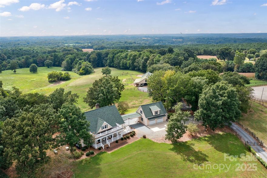 A remarkable equestrian estate on more than 29 acres, this Southern Living home reflects a thoughtful connection to land and lifestyle. Privately sited at the end of a gated drive, the residence features wraparound porches and expansive decking that embrace the surrounding farmland. The main house offers 10-foot ceilings, hardwood floors, custom trim, and abundant natural light through French doors and tall windows. A floor-to-ceiling stone fireplace anchors the cathedral-ceiling great room, with seamless flow into the keeping room, kitchen and breakfast area. The chef’s kitchen showcases knotty pine cabinetry, stainless-steel appliances, quartz countertops, a walk-in pantry, built-in desk and built-n bench with breakfast table.  The main-level primary suite includes a spa-inspired bath, soaking tub, large frameless shower and oversized walk-in closet, with plumbing updated in 2026. Upstairs are two guest suites, private baths, walk-in closets and a flexible bonus room. Plenty of storage space.
A breezeway connects the main home to a 2022 two-car garage with upper-level living space (was permitted as an office with bathroom). A separate gated drive leads to a European-style barn with 14 matted stalls, two convertible broodmare stalls, wash station, heated tack room, heat lamps for wash stall, feed room, office, and walk-up hayloft. Additional equestrian amenities include five fenced paddocks, a covered run-in w/storage, a round pen and a professional-grade 125’ by 225’ arena. RV hook up near the home, equipment storage attached to the barn, full house generator and a tall crawl space with dehumidifier are just a few of the additional features.
Offering privacy, functionality and timeless charm, this estate is a rare opportunity for equestrian enthusiasts seeking a blend of tradition and modern comfort. Sunsets over the pastures will take your breath away will keep your camera clicking away.