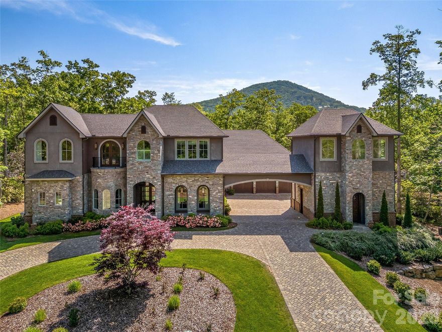 Experience luxury mountain living at its finest in The Cliffs at Walnut Cove, Asheville’s premier private golf and wellness community. Perfectly positioned within half a mile of The Golf House & Tavern, this extraordinary modern estate blends sophisticated design, master craftsmanship, and timeless elegance. Completed in 2019, 1905 White Tree Trail rests gracefully on a beautifully landscaped 1.24-acre corner lot surrounded by natural beauty and mountain serenity. Boasting more than 6,000 square feet of thoughtfully designed living space, this custom-built masterpiece combines contemporary architecture with warm, natural materials that harmonize with its surroundings. The open-concept layout seamlessly connects the living, dining, and kitchen areas, offering both functionality and flow for entertaining and everyday living. At the heart of the home, the Great Room makes a lasting impression with its soaring 25-foot ceilings and dramatic floor-to-ceiling wall of windows that flood the interior with natural light and showcase the tranquil outdoor scenery. A stunning see-through fireplace provides an elegant connection between the dining room and office, creating an atmosphere that is both grand and inviting. The gourmet kitchen is a true showpiece, featuring custom cabinetry, exquisite woodwork, and top-of-the-line appliances including a Wolf double oven, multi-burner gas cooktop, and an impressive side-by-side refrigerator and freezer. Waterstone faucets and a well-appointed butler’s pantry elevate the culinary experience, while expansive counter space makes this kitchen ideal for hosting gatherings of any size. The main-level primary suite serves as a private sanctuary, complete with a cozy fireplace, spa-inspired bath featuring a freestanding slipper tub, glass-enclosed shower, and dual backlit custom closets designed for both elegance and organization. A main-level guest suite offers privacy and comfort for visitors, with a beautifully appointed en-suite bath that mirrors the home’s refined design aesthetic. Upstairs, the home continues to impress with a bright sitting area, two spacious bedrooms, a full bath with dual vanities, and a generous bonus room perfect for a gym, studio, or hobby space. The dedicated media room provides the ultimate retreat for movie nights or sporting events, while a unique two-story tower adds architectural distinction and endless possibilities for customization; such as a reading nook, art space, or private office. Every detail of this residence reflects a commitment to quality and design excellence, from the precision of its craftsmanship to the selection of premium finishes. The three-car garage offers abundant storage, while the expansive lot provides room for outdoor living, entertaining, or even future enhancements such as a pool, outdoor kitchen, or garden oasis. Residents of The Cliffs at Walnut Cove enjoy membership opportunities to a world-class array of amenities, including a championship Jack Nicklaus Signature golf course, state-of-the-art wellness center, indoor and outdoor pools, tennis and pickleball facilities, and an impressive network of hiking trails that wind through the community’s preserved natural landscape. Membership at The Cliffs also provides access to all seven Cliffs communities across the Carolinas, offering a truly elevated lifestyle experience. Located less than eight miles from the Asheville Regional Airport and just minutes from the vibrant culture and fine dining of downtown Asheville, this modern estate offers the perfect balance of tranquility, luxury, and accessibility. Experience refined living, masterful design, and the unmatched beauty of Western North Carolina at 1905 White Tree Trail — a home where modern elegance meets mountain serenity. Book your showing today!