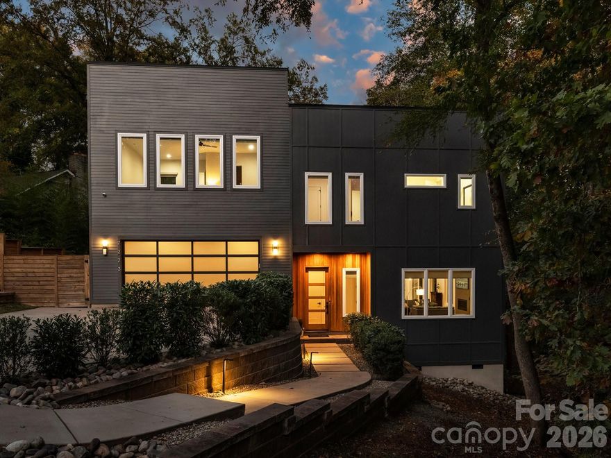 Modern luxury meets elevated indoor-outdoor living in a private setting in Stonehaven. With ten-foot ceilings and high-end finishes throughout, this home’s striking architectural design is crafted for both elegant entertaining and everyday comfort. Set beautifully into its half-acre wooded lot, the home is surrounded by peaceful views that create an immersive outdoor experience. The open floor plan flows seamlessly to over 700 square feet of Ipe wood wrap-around deck, positioned among the trees and offering exceptional privacy. A gas fireplace on the deck enhances comfort on cooler evenings, while a fully enclosed fenced turf side yard provides privacy and a space for pets to enjoy. The wooded landscape invites exploration and enjoyment- ideal for outdoor play or evenings gathered around a fire pit beneath the canopy. The chef’s kitchen is beautifully appointed with a built-in Sub-Zero refrigerator, ZLINE gas range with hood, Bosch dishwasher, dual temperature-controlled wine fridges, microwave drawer, and a dramatic waterfall island ideal for gathering. Two walls of sliding glass doors create a seamless transition between interior and exterior spaces. Inside, a gas fireplace adds warmth and ambiance to the light-filled main living area. Thoughtful SMART home systems control heating and cooling, fireplaces, garage door, irrigation system, Sub-Zero refrigerator, EV charger, and a high-end security system. Blonde white oak flooring leads upstairs to a luxurious primary suite featuring tranquil views, two custom closets, and a spa-inspired bath with zero-entry rain shower, hand shower, soaking tub, and dual quartz vanity. Three additional bedrooms with custom closets and two beautifully finished baths complete the level. The upper level includes a cozy reading nook and an expansive bonus room that may serve as a fifth bedroom with its own full bath. Ideally located near James Boyce Park, Sardis Swim & Racquet Club, McAlpine Creek Greenway, and several private schools, this is refined living defined by privacy, light, and architectural refinement. Welcome home.