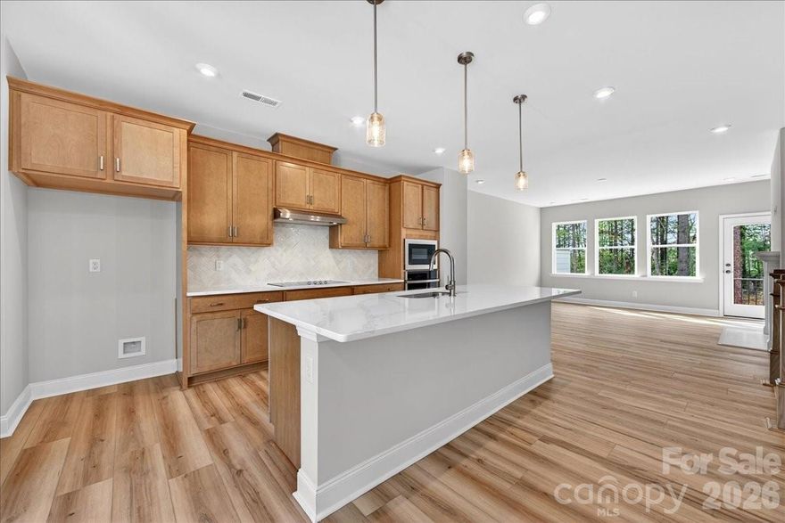 Just released in our sought-after model row, this beautifully designed townhome blends warmth, style, and functionality. From the moment you arrive, you’re welcomed by charm. The entry level features a convenient drop zone off the garage and a private guest suite with EVP hardwood flooring, a full bath, and a tiled shower. Step outside to a private first-level back patio overlooking peaceful wooded views. At the heart of the home, the gourmet kitchen showcases warm saddle brown cabinetry, quartz countertops, and an oversized walk-in pantry. Natural light pours in, enhancing the inviting tones and creating a space that feels both cozy and elevated. The kitchen flows seamlessly into the open-concept great room, featuring a sleek electric fireplace with crisp white trim and access to a second-level outdoor living area. White railing details along the stairs add a bright, modern contrast throughout. Upstairs, unwind in the expansive primary suite, complete with a spa-like bath featuring warm cabinetry and floor-to-ceiling tile, offering timeless style with low-maintenance durability. With designer finishes, flexible living spaces, and a welcoming, elevated feel throughout, this home won’t last long.