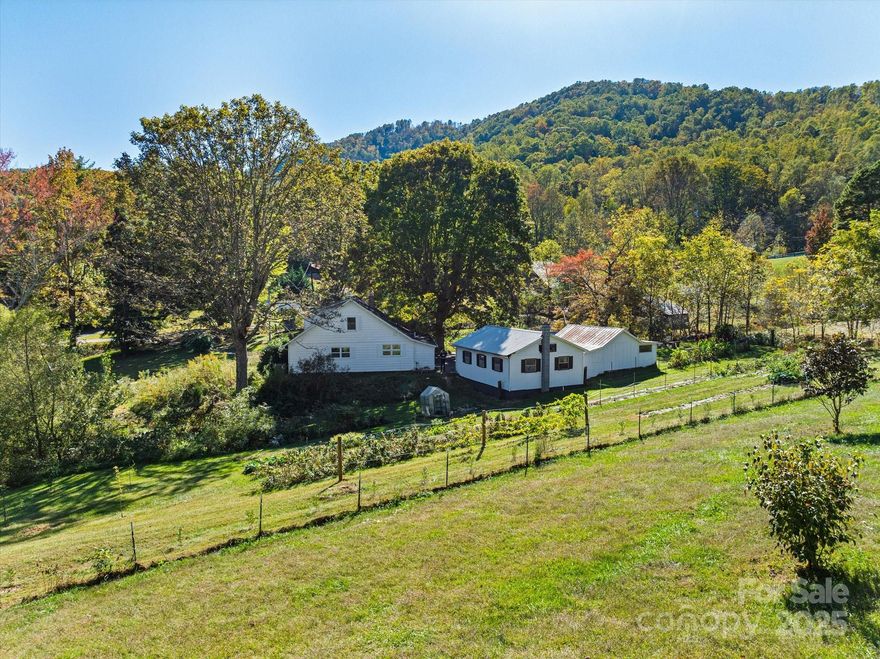 This idyllic 1924 farmhouse sits on 1.4 mostly cleared acres with two year-round creeks and fed by an impressive spring that provides a steady source of fresh water. Grow your own food and flowers in the large, established organic garden—or simply enjoy the harvest from the existing fruit trees and bushes, including blackberries, blueberries, peaches, pears, apples and more! The property offers many inviting spaces to unwind—relax in the shade beside the koi pond, visit the chickens beneath the old oak trees, or gather around a bonfire under the stars. The home features two welcoming porches and numerous recent updates, including the addition of a full bathroom off the primary bedroom. With four bedrooms plus an office or den, the layout offers flexibility and privacy—ideal for shared living, guests, or creative workspace needs. The three bedrooms/bonus rooms upstairs are just under 7' in ceiling height and do not contribute to the total HLA. There is also a detached garage with electricity and a wood-burning stove, great for projects, and a large shed for additional storage. Enjoy peaceful living with easy access—nestled in a quiet setting along a gently rolling paved road, just five minutes from the Blue Ridge Parkway and Ingles on Charlotte Highway, and only ten minutes to downtown Asheville! Check out the property website for a virtual tour, garden map, and more photos!