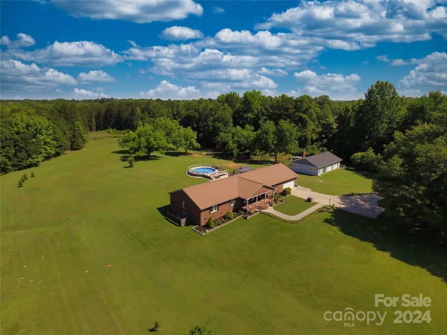 Peaceful sanctuary w/14+ acres less than 10 min. from shopping, dining, & more. Enjoy a front porch sunrise or back deck sunset w/gazebo covering and separate grill station piped w/natural gas. Private semi in-ground pool w/deck & dusk to dawn lighting.  2+ acres fenced pasture w/3 stall run-in & storage area plus 3 add’l pens.  Run-in shed has electric w/separate meter. Upfront pen has lights, elec.& metal roof. RV hookup at run in. 1500 sq ft 3-car  w/one bay heated/cooled flex space. Add’l  2 bays contain built-in bench & pull down. Nearly 3000 sq full brick ranch w/metal roof & 810 sq attached 2 car garage features tile, led fixtures, new carpet, solid wood doors, walk-in hall closet, & oversized linen closet.10x10 custom closet adjoins 20 x 20 primary bed plus en-suite. Custom kitchen cabinets, pantry wall & pullouts. List of upgrades & floorplan in photos –HVAC, new windows, tankless, 3 car roof & more. Sit down-stay a while, your dream home is here!  Sellers licensed Realtors.