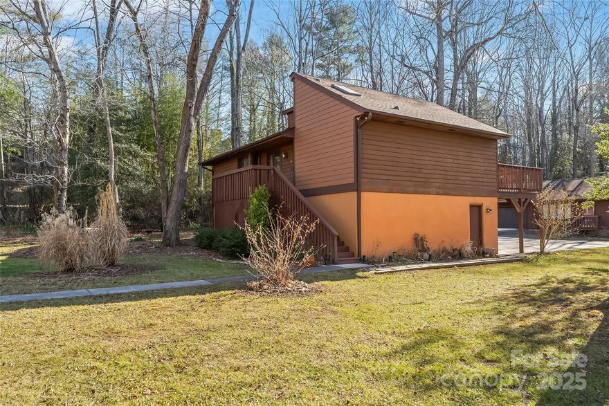 NOW OFFERED BELOW TAX VALUE! Don’t miss this rare opportunity to own one of the most desirable homes in Wildwood Gardens. Perfectly positioned at the end of the street with no thru traffic, this well-maintained home offers a level .26-acre yard in a beautiful, serene natural setting. The home features three bedrooms, each with its own full en-suite bath, along with an attached double garage—a combination that truly checks all the boxes! Inside, the open-concept living and dining area impresses with a vaulted ceiling, stone-framed gas log fireplace, and easy access to an extended deck that provides partial coverage over the driveway below. The thoughtfully designed floor plan features split bedrooms on the main level, plus a private, updated third bedroom on the lower level with separate entrance, making this home ideal for short-term or long-term rentals, guests, or multi-generational living. The primary suite includes a walk-in closet and a spacious updated bath with a newer glass shower door. The laundry area has been relocated to the main level for added convenience. Improvements include a newer roof and gutters, central AC, and electric range. The flat, green yard is a standout feature, enhanced by blooming plants in warmer months. Enjoy peaceful views of the park-like setting from the front porch or back deck, including a gently flowing nearby creek with a charming arched bridge that adds to the tranquil atmosphere. No storm damage or water intrusion from Helene. While the property is located in a 100-year flood plain, it has not flooded during the sellers’ ownership since 1989. HOA dues are just $105 per month and include lawn maintenance, private road maintenance, snow removal, and even tree care beyond a 5-foot perimeter of the home. $2,000 special assessment already paid by seller. Conveniently located between Asheville and Hendersonville, offering easy access to shopping, dining, and everyday amenities—this is a special home at an exceptional value.