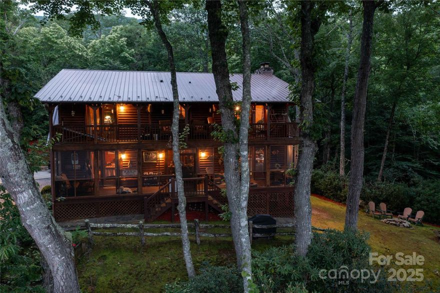 At the edge of Pisgah National Forest, this almost 3200 ft elevation luxury mountain retreat with its private waterfall and creek is a breathtaking oasis. Warmth and sophistication abound. With vaulted, exposed beam ceilings that feature a great room stone fireplace, a spacious custom kitchen with a large island, and high-end appliances, this home is perfect for family and entertaining. Retreat to the primary suite with its access to a screened porch and spa-like bathroom with a soaking tub and walk-in shower. Upstairs, two large bedrooms and a bathroom share a covered deck with scenic mountain views. A large garage can double as a workout space and easily accommodate ATVs, fishing, and golf equipment. This living work of art is a HOME where every turn tells a story of nature and craftsmanship. Enjoy the fire pit and grill outside, cozy up inside, and fall asleep to the gentle melodies of the waterfall and creek. This is where luxury and wilderness blend for idyllic mountain living.