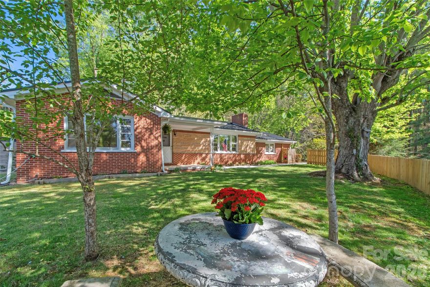 This charming 3BR, 2BA brick home built in 1965 perfectly blends mid-century character w/modern updates. Step inside to discover 1,504 sq. ft of comfortable living space featuring original hardwood floors throughout and a stunning living room fireplace accented by unique pink/purple stone sourced from an East Tennessee quarry. The kitchen is fully equipped with stainless steel appliances and flows seamlessly into the dining area. Recent improvements include a new metal roof installed in 2024 and new gutters in 2025. Both the guest bathroom and the primary suite bathroom have been recently renovated adding a fresh, modern touch to this well-loved home.
The property offers versatility starting w/the spacious converted 2-car garage. Currently set up as an inspiring art studio w/electrical hookups for two pottery or glass kilns, this space offers the flexibility to remain an artist's haven or could be easily transitioned back into a traditional garage. The full basement provides ample extra space for all your storage needs. The .56-acre lot is a true sanctuary surrounded by fruit trees, native perennials & established flower beds. The grounds feature a unique walking labyrinth patio, raised garden beds & a relaxing trellis swing all set against the backdrop of sunset & mountain views. Located in the heart of Burnsville, this home is just moments from everything you need. Conveniently positioned near Hwy 19E you're only 5 mins to Burnsville Elementary, East Yancey Middle and Mountain Heritage High School. Burnsville is a vibrant town nestled in the Blue Ridge Mountains & serves as the gateway to Mount Mitchell the highest peak East of the Mississippi. Enjoy an easy 30 min commute to Asheville while having immediate access to local hiking trails, a lively downtown with a thriving art community & stargazing opportunities at the Bare Dark Sky Observatory. Don't miss the chance to experience this unique slice of mountain paradise!