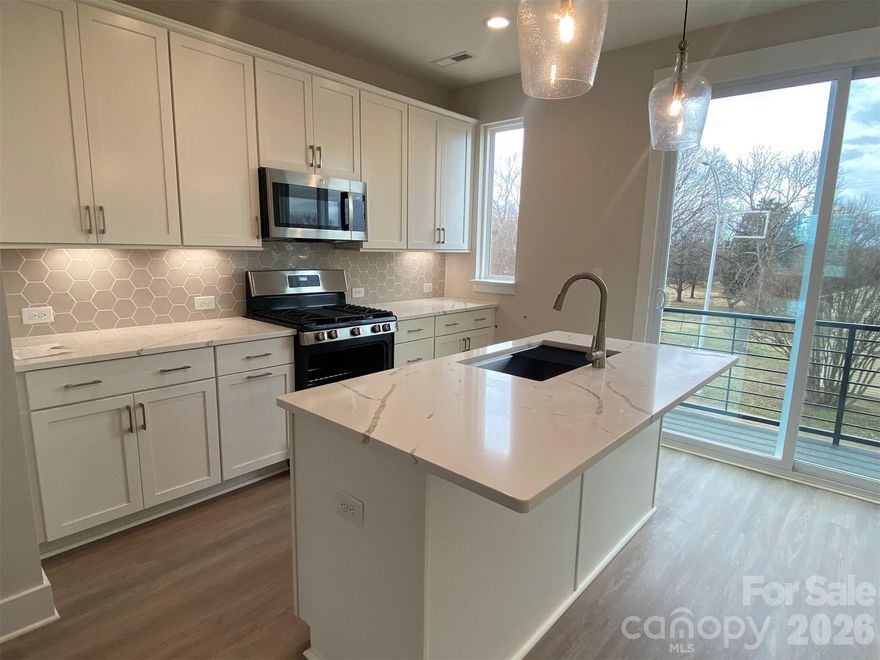 Enjoy abundant living space in this end-unit townhome, walking distance to Camp North End. Seasonal city skyline views from the kitchen terrace! 1-car garage plus driveway parking, 1st floor flex rm w/  powder, 4th floor bonus bedroom w/ powder, & a spacious rooftop terrace. Nice open layout on the 2nd floor. Kitchen has 42" white cabinets w/ satin nickel hardware, quartz counters, pantry cabinet, LED under-cabinet lights, trash pullout, large SS undermount sink, and GE SS app w/ gas range. 3rd floor hosts the laundry closet w/ tiled floor & both bedrooms. Premier bath includes quartz counters, white cabinets, tiled floor, & tiled shower with semi-frameless glass. Guest bath has white cabinets, quartz counters, and tiled floor. Satin nickel hardware in baths. LVP floors throughout 1st & 2nd floors & 3rd floor landing, with oak treads on all stairs. Tile floors in half baths on 1st & 4th floors. 3 ceiling fans included plus 9' ceilings.