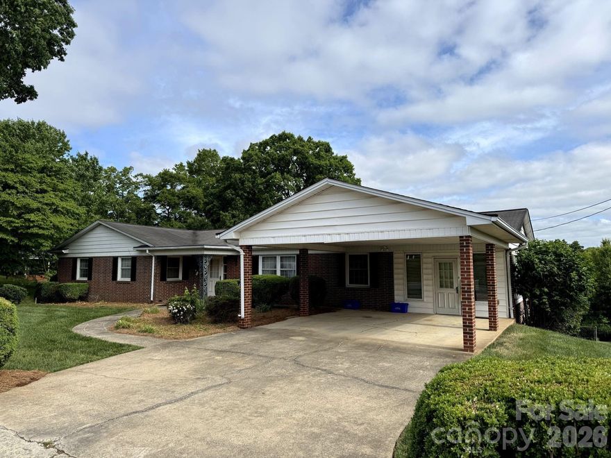 Well-maintained Brick Ranch with a full, partially finished Basement located in Granite Falls. The home features original hardwood floors throughout much of the main level, with updated flooring in the den, kitchen, family room, and heated basement area. The main level includes a kitchen and den combination, sunroom, living room with fireplace, primary bedroom, two additional bedrooms, and two full bathrooms. A cozy family room is located near the entrance from the attached double carport, as well as the home including a spacious laundry room. The full basement offers a bar area, unfinished full bathroom, and a large open space suitable for recreation. A second fireplace with wood stove insert is also located in the basement. Exterior features include a well-maintained in-ground pool, covered brick patio, 12' x 16' deck, and a garage door providing access to a workshop area. The existing chain-link fence represents an approximate property boundary. Buyer to verify all property lines and features.