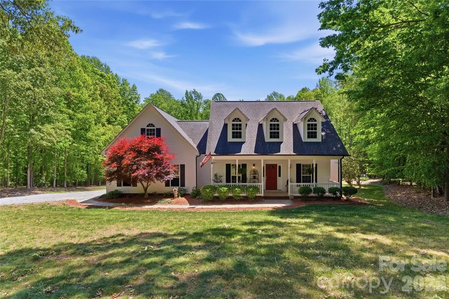 Situated on 3.51 private, wooded acres just minutes from downtown Waxhaw’s charming historic district, this one-owner home has been well maintained and offers a rare blend of privacy, space, and lifestyle—close to shops, restaurants, and local events, yet quietly tucked away from it all.

A welcoming covered front porch—anchored by a charming entry and striking red front door—sets the tone as you arrive, leading into a thoughtfully designed home with a functional and inviting layout. The main living area is open and welcoming, with a vaulted ceiling, warm wood floors, a great room with fireplace, and a seamless flow into the dining area and kitchen—ideal for both everyday living and entertaining. The kitchen is filled with natural light and features abundant wood cabinetry and generous counter space, all at the heart of the home.

A desirable split-bedroom floor plan provides privacy, with the primary suite on one side, featuring a spacious private bath complete with a soaking tub, walk-in shower, and a large walk-in closet. Two additional bedrooms are located on the opposite side with a full bath in between.

Upstairs, two versatile bonus spaces offer flexibility for a variety of uses. One is a private room with its own half bath—perfect as a bedroom, guest room, office/flex space, or second living area—while the open bonus area, currently used as a sewing room, would make an excellent home office, media room, artist studio, or additional living space. The attached 2-car garage has finished walls and an additional storage closet, adding everyday convenience and functionality.

Step outside and the property truly stands out! The private backyard is designed for both relaxation and entertaining, featuring a full-length covered back porch that overlooks an expansive stone terrace/patio and in-ground swimming pool. The stone terrace adds warmth and character, creating an inviting space to gather, unwind, and enjoy the peaceful, wooded setting.

The in-ground pool becomes the centerpiece of outdoor living during the warmer months—perfect for hosting summer parties, weekend cookouts, or simply enjoying a quiet afternoon by the water. With plenty of room for lounge seating, dining, and entertaining, this backyard offers a seamless blend of comfort and functionality, making it ideal for both intimate evenings and larger gatherings.

Beyond the immediate backyard, the land opens up to a beautiful natural setting with a creek along the rear of the property. With usable acreage and a mix of open and wooded space, this property is well-suited for a variety of lifestyles— including keeping chickens, maintaining gardens, as well as horses and other livestock. A small outbuilding with fenced area is currently serving as a storage building with a small dog house and fenced dog yard. This would also make an excellent chicken coop.

In addition to the main home, there is a two-car carport and a detached 3-car garage. Two bays of the garage function as a traditional garage space, while the third bay has been finished as a man-cave with bar and upgraded interior—ideal for hobbies, entertaining, or a separate retreat. (bar is removable - but may stay if buyer desires).

With acreage, privacy, no HOA and a location just minutes from the heart of Waxhaw, this is a rare opportunity to enjoy both convenience and country living.