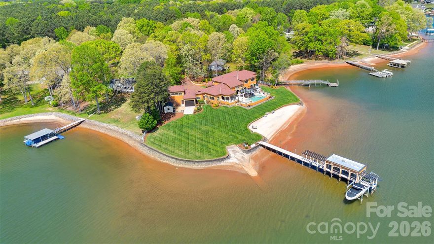 A truly rare offering on Lake Norman, this extraordinary Mediterranean-inspired waterfront estate is privately positioned behind gates on nearly an acre, showcasing approximately 500 linear feet of shoreline and a natural sandy beach—an exceptional combination that creates both dramatic presence and effortless lakefront living.
Designed to capture breathtaking sunrise-to-sunset panoramic water views, the residence blends timeless architecture with resort-style amenities and remarkable privacy. Expansive terraces and outdoor entertaining areas create a seamless connection between elegant interiors and the beauty of the lake beyond.
At the heart of the home, the oversized gourmet kitchen featuring three sinks is thoughtfully designed for both everyday living and large-scale entertaining, offering generous workspace and effortless flow into the main gathering spaces. Each bedroom is appointed with its own private ensuite bath, creating a true retreat experience for both residents and guests. Adding exceptional flexibility, the property also features a private studio apartment located above the oversized garage and RV bay, complete with its own full kitchen and washer/dryer hookup—ideal for extended family, visiting guests, multigenerational living, or a private executive-style workspace with separation from the main residence. Outdoor living reaches another level at the private pier, which serves as its own lakeside entertaining destination, complete with a built-in dockside kitchen featuring a sink, BBQ, griddle, refrigerator, and ice maker. Two boat lifts provide convenient access for multiple watercraft, making spontaneous days on the lake beautifully effortless. Collectors and adventure enthusiasts will appreciate the oversized garage with a dedicated third-bay RV garage, offering exceptional space for vehicles, boats, and recreational equipment.
Set behind a private gated entrance with no HOA restrictions, this estate offers a rare combination of privacy, flexibility, and shoreline scale that is increasingly difficult to find on Lake Norman. The expansive waterfront setting, sandy beach frontage, and sweeping views create an unforgettable sense of arrival and a lifestyle defined by both elegance and recreation. From sunset gatherings along the shoreline to mornings launching directly from your private pier, every element of this residence reflects intentional design and effortless luxury. With remarkable shoreline presence, Mediterranean architectural character, dual boat lifts, a fully equipped dockside kitchen, private guest quarters above the RV garage, ensuite accommodations throughout, and unmatched privacy, this exceptional Sherrills Ford waterfront estate represents a rare opportunity to own a true Lake Norman legacy property.