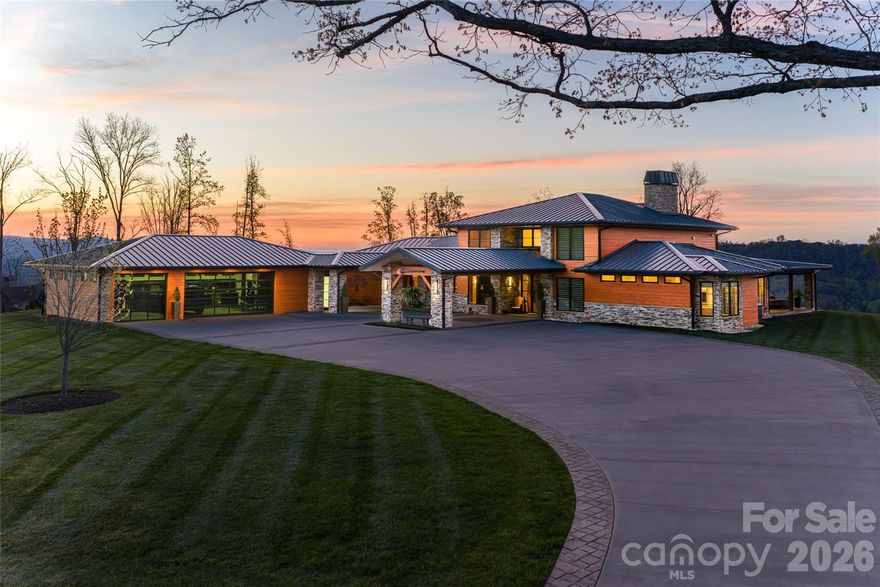 Set along a scenic ridge in the heart of pristine Reems Creek Valley, 170 Bear View Road presents a rare combination of refined luxury, effortless one-level living and breathtaking long-range views from every room. Ideally positioned to capture the surrounding Blue Ridge landscape, this private and gated mountain estate offers an exceptional sense of space and tranquility while remaining just minutes to the charm of downtown Weaverville and a short drive to the vibrant dining, arts and cultural scene of Asheville. Thoughtfully designed with an emphasis on craftsmanship and elevated finish, the home unfolds with hardwood floors throughout and a light-filled, open-concept layout anchored by a dramatic great room and chef’s kitchen. A gracious foyer leads into the main living space, while a formal dining room to the left is defined by a striking stone accent wall and soaring double-height ceiling, an ideal setting for intimate dinners and large-scale entertaining. The kitchen is a centerpiece, curated for everyday living and culinary excellence. A wraparound granite island with integrated storage anchors the space, complemented by premium appliances including a Sub-Zero built-in refrigerator and freezer, BlueStar six-burner gas cooktop with griddle, double wall ovens, Wolf microwave and warming drawer, and a full wine and coffee station. Copper sinks, custom cabinetry and a thoughtfully designed walk-in pantry, complete with prep counters, secondary refrigeration and filtered water system, underscore the home’s exceptional attention to detail. Privately situated, the primary suite occupies its wing, offering a serene retreat with a stone and wood-accented fireplace, dual custom walk-in closets, and a spa-inspired bath featuring copper vanities, a freestanding stone soaking tub and a tiled walk-in shower with dual heads. Three additional guest suites, each with en-suite baths, are thoughtfully positioned within a split-bedroom layout, providing comfort and privacy for family and guests alike. A double-height office with custom built-ins, designer finishes, and sliding barn doors creates a distinctive and inspiring workspace, while the mudroom and laundry area, complete with a built-in dog washing station and direct access to the breezeway, adds function and convenience. Outdoor living is equally compelling, with a covered rear porch designed for year-round enjoyment. Anchored by a wood-burning stone fireplace and finished with durable hardwood decking, this space extends seamlessly to an integrated hot tub, all oriented to take full advantage of the sweeping mountain views. The property also features a porte-cochère, irrigation system, and a detached, climate-controlled three-car garage with a fully outfitted gym space and half bath, offering flexibility for a variety of lifestyles. With its combination of elevated design, meticulous attention to detail, expansive mountain views and proximity to some of Western North Carolina’s sought-after destinations, 170 Bear View Road represents an exceptional offering in the Asheville area luxury market.