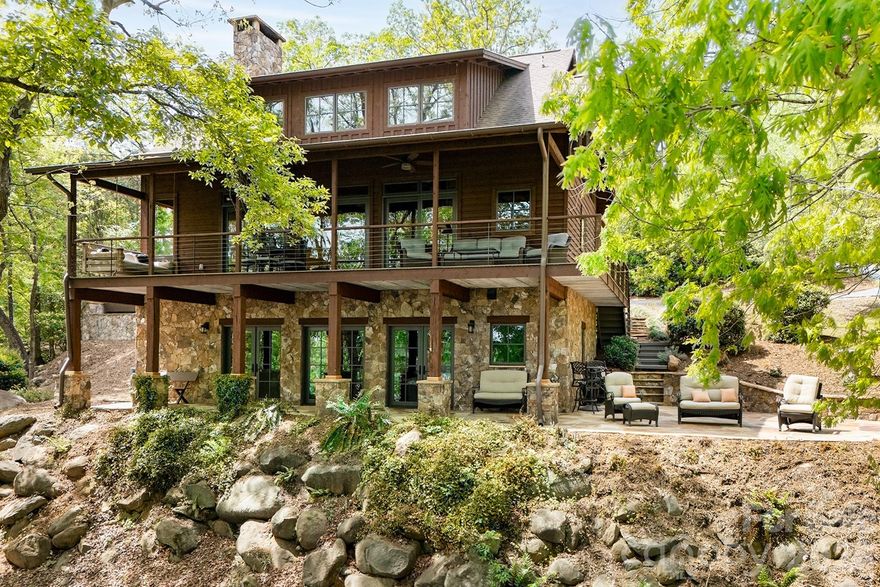 Stunning Fully Furnished Custom Lakefront Retreat with Luxury Rustic Design & Exceptional Outdoor Living!

Experience the perfect blend of craftsmanship and comfort in this one-of-a-kind lakefront home, offered fully furnished for a true turnkey opportunity. Every detail has been thoughtfully curated, showcasing high-end finishes and timeless rustic elegance throughout.

From the moment you enter, you’re greeted by soaring cathedral ceilings with massive exposed wooden beams in the expansive great room, seamlessly connecting the living, dining, and kitchen spaces. A striking wood-burning fireplace wrapped in dry-stack stone and exposed on all sides serves as the centerpiece, while three sets of oversized sliding glass doors with six panels flood the home with natural light and frame breathtaking lake views.
The gourmet kitchen is a showstopper, featuring custom stained oak cabinetry, leathered and chiseled granite countertops and backsplash, a large island with bar seating, stainless farmhouse sink, and an electric cooktop with a sleek telescopic downdraft system.

The main-level primary suite is a private sanctuary with wood flooring, walls, and ceiling, built-in closets, and a spa-inspired bath complete with a custom tile shower, pebble flooring, dual shower heads, built-in bench, custom glass door, cabinetry, and chiseled-edge granite finishes.

Upstairs, a loft-style bedroom offers exceptional character with wood floors, walls, and ceilings, a barn door for privacy, built-in storage, and a private balcony overlooking the great room and lake. The full bathroom continues the elevated design with custom cabinetry, leathered chiseled granite countertops, and a beautifully tiled shower with pebble flooring, custom glass door, and tile bench.

The fully finished basement expands the living space with a warm den featuring insulated tin ceilings with wooden beams, tile flooring, and a wood-burning dry-stack stone fireplace with wooden mantle. Additional spaces include a versatile bonus room with built-in furniture and storage, a spacious bedroom/bunkroom with tin ceilings and atrium door access to a covered patio overlooking the water, and a full bathroom with double vanity, countertop-mounted sinks, vintage-style fixtures, and a custom tile shower.

Step outside to an entertainer’s dream. The outdoor pavilion showcases cathedral ceilings with large, exposed beams and features a fully equipped bar with chiseled-edge granite countertops, stainless refrigerator, dishwasher, large sink, Blackstone grill top, custom shelving, and rustic cabinetry with black hardware. The expansive hand-laid flagstone patio overlooks the water and is complemented by a stone retaining wall, picnic area, Adirondack seating, and custom wood barstools. Enjoy the outdoor shower, oversized hot tub with lake and wooded views, and a hand-laid stone fire-pit surrounded by luxury outdoor furniture.

The impressive boathouse (approximately 1,200 sq ft) is beautifully finished with wood flooring, completed ceilings with can lighting, custom cabinetry, butcher block countertops, cedar walls, built-in storage, and multiple seating areas including bar and lounge space—ideal for relaxing or entertaining at the water’s edge.
Additional highlights include rustic stained cedar siding with individually cut cedar shakes, red oak hardwood flooring, white pine walls, spruce pine ceilings, a covered lakeside porch with tongue-and-groove yellow pine flooring, insulated tin basement ceilings, and a concrete driveway with parking for seven or more vehicles. The property is enhanced by mature, mountain-inspired landscaping with cherry trees, magnolia trees, and Japanese maples, along with a stone walkway, wooden steps, and a gravel cart path leading to the boathouse.

This extraordinary property offers unmatched lakefront living with refined rustic luxury—fully furnished and ready to enjoy from day one.