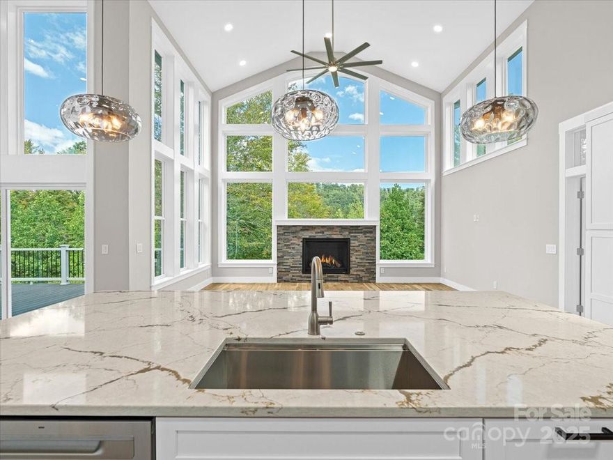 The stone-wrapped porch and transom-lit foyer open to a dramatic reveal: a 16-foot wall of dining room glass overlooking the private greenway and forest beyond. Just beyond, the vaulted great room unfolds, its 19-foot peaks and three walls of glass framing the woods and sky around a grand centerpiece fireplace. The effect is at once expansive and intimate, a place that feels like a retreat yet is designed for everyday living.

Outdoor living is central here. Eight-foot patio doors with tall transoms border the dining room on two sides—one opening to a 23-foot open deck, the other into a soaring 12×18 screened porch with wood-stained ceiling. This year-round room blurs the line between indoors and nature, the perfect setting for mountain sunsets or quiet mornings.

At the heart of the home, the chef’s kitchen centers on a quartz-topped island nearly five by ten feet. A sleek L-shaped run of full-depth white cabinetry sets the tone, balanced by a suite of LG stainless appliances including a six-burner gas cooktop, convection wall oven with micro/air fry, wine cooler, counter-depth refrigerator, and whisper-quiet dishwasher. Above, the glass-railed balcony of the upper family room adds vertical drama while connecting the spaces together.

The main level also includes two bedroom suites. The vaulted primary is filled with light from sky windows, with dual custom closets leading to a spa-inspired bath finished in porcelain tile, soaking tub, seated glass shower, and an expansive custom vanity. The second ensuite flex room offers its own privacy and mountain views.

A skylit oak stair rises to the upper level, where the lofted family room overlooks the great room and distant ridgelines. A full bath and additional bedroom or office complete this floor.

The daylighted lower level is equally versatile: a 19×26 family room with kitchenette, two bedrooms with walk-in closets, and two full baths including one ensuite. Wrapped by patios and decks, this level connects seamlessly to the outdoors.

Efficiency matches beauty. Triple-zoned HVAC with a Bosch variable-speed heat pump, advanced 2×6 gasketed exterior walls, engineered floor and roof trusses, radon mitigation, and architectural roofing are all third-party verified through Energy Star and Duke HERO programs. Certifications confirm performance, comfort, and lower utility costs.

Greenwood Park and sister community Reems Creek Village together form a neighborhood nearly 25 years in the making. Across from Reems Creek Golf Club, the community is known for quiet streets without through traffic, distinctive custom homes, and welcoming neighbors. Private roadways loop through breathtaking views—south and east to the Blue Ridge Parkway, west to Pisgah and the Smokies, and north to Hamburg Mountain. Two miles to downtown Weaverville, 15 minutes to Asheville, 10 minutes to the Parkway, and near a newly approved hospital site, the location blends small-town charm with regional access.

This home is now under contract. A similar new home with comparable finishes and design is nearing completion within Greenwood Park. Contact listing agent for details or to arrange a preview before it’s listed.

Explore the home anytime with the self-guided 3D tour—see Virtual Tour Link.