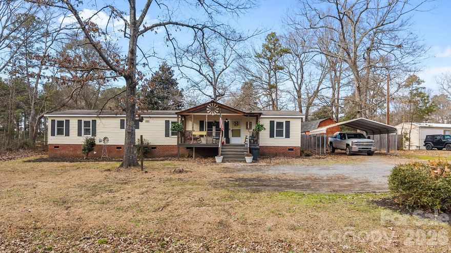 Charming single-story manufactured home offering an open-concept layout with character and functionality throughout. The spacious main living area features durable vinyl plank flooring, ceiling fans, and a cozy fireplace, flowing seamlessly into a large kitchen and dining space ideal for everyday living and entertaining. The kitchen offers ample cabinetry, stainless steel appliances, generous counter space, and a large island with seating and hanging pot rack.
The home offers four bedrooms, including a generously sized primary bedroom with space for a sitting area and convenient access to the full bathroom featuring a dual-sink vanity and tiled walk-in shower. The additional bedrooms provide flexibility for use as guest rooms, home offices, hobby spaces, or storage as needed.
Enjoy outdoor living on the expansive covered and screened porch—perfect for relaxing or entertaining year-round. The fenced backyard includes a detached storage building/workshop and room to personalize. Covered front porch, carport, and additional parking complete the property. Situated on a spacious lot with mature trees, offering privacy and versatility. Title has been retired, and septic system was pumped in the past year.