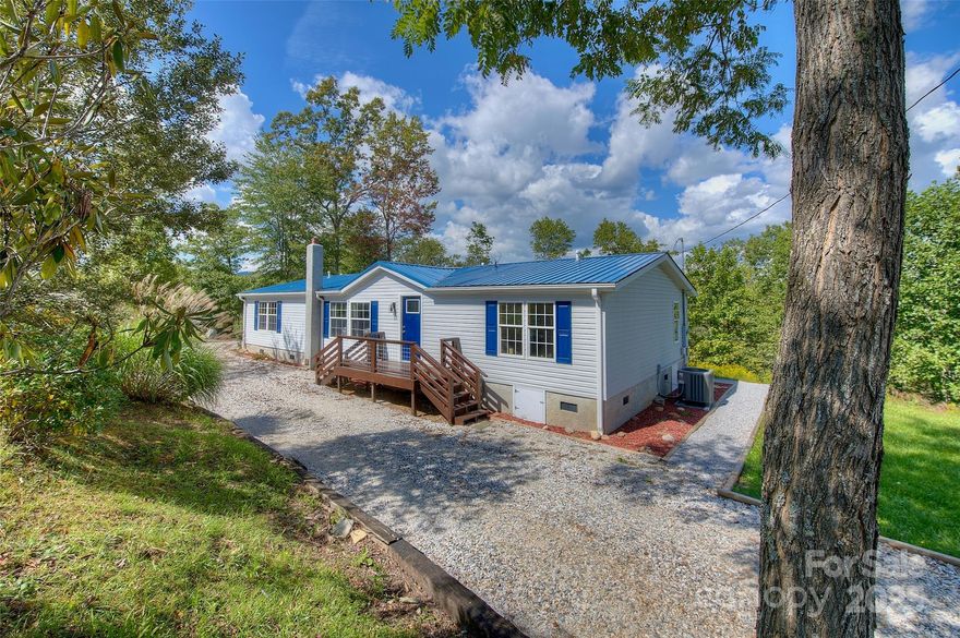 LIKE NEW—FULLY UPDATED! Four-bedroom, two-bath manufactured home in a private, picturesque setting with stunning mountain views. Features city water, new (2025) central HVAC, light blue tent siding, blue shutters, and a spacious wooden deck with sturdy staircase. Brand new (2025) metal roof! Large windows flood the interior with natural light, showcasing rolling hills and distant mountains. Includes a circular gravel driveway, detached metal garage, mature trees, and lush landscaping for privacy and tranquility, yet close to local amenities. Your perfect mountain getaway in the heart of Appalachia and Blue Ridge!
The living room is warm and inviting with rich flooring, vaulted ceiling with wood paneling, and large windows with neutral curtains for abundant light and stunning views. Furnished with a plush sofa, armchairs, and coffee table, it’s perfect for relaxation or gatherings. A screened-in porch extends the living space, blending indoor comfort with nature’s beauty.
The kitchen is functional and charming with warm wood cabinetry, sleek black hardware, and butcher block countertops. A stainless steel double sink sits beneath a large window with mountain views, complemented by a spacious island with pendant lighting for prep and casual dining. Appliances blend stainless steel and classic finishes for style and practicality.
The master bedroom ensuite offers relaxation with warm wood flooring, vaulted ceiling with wood paneling, and a ceiling fan. A large bed with plush bedding, matching nightstands, and stylish lamps create a cozy ambiance. Large windows provide natural light and scenic views. The ensuite bathroom features a jetted tub with marble-inspired walls, wood accents, dual-sink vanity with marble countertop, and a glass-enclosed shower, all meticulously designed.
Guest bedrooms are versatile and inviting. The first, near the master, is bright with large windows and mountain views, ideal as a nursery or office. The second and third bedrooms offer similar charm with expansive windows and a serene atmosphere. They share a well-appointed bathroom with a modern vanity, wood countertop, and tub/shower combo, ensuring guest comfort with neutral tones.
The outdoor screened-in deck is a highlight, offering breathtaking Blue Ridge Mountain views. Accessible from the living area, it features a sturdy wood floor, screen panels for fresh air, a ceiling fan for comfort, and natural wood railing with ambient lighting. Perfect for relaxation or entertaining with panoramic vistas of rolling hills and distant peaks.
Your home for weekends or a lifetime! Located 3 min to downtown Spruce Pine, 2 min to Blue Ridge Regional Hospital, 1 min to Mayland Community College, 5 min to Blue Ridge Parkway, 20 min to Burnsville, Marion, Lake James, and I-40, 35 min to I-26 and Mars Hill, 50 min to Asheville and Boone, 60 min to Johnson City, TN, and 2 hrs to Charlotte, NC.