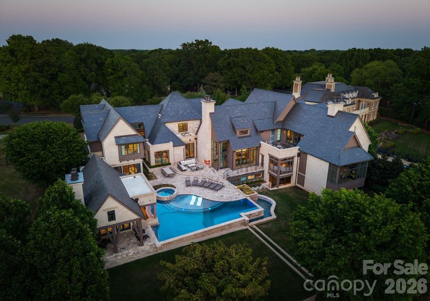 Set along the championship fairways of Quail Hollow Club, host to the city's most prestigious PGA tournaments, 7318 Baltusrol Lane is one of the most exquisite custom homes ever offered in Charlotte. Encompassing 17,843 square feet of heated and cooled living space, this 6 bedroom, 6 full bath, and 6 half bath estate was built in collaboration with architect Harry Schrader, Arcadia Homes, and J Layton Interiors.
Clad in 4" hand-cut limestone and framed by lush landscaping and lighting, the estate's exterior commands immediate reverence. A grand porte-cochère anchors the gated motor court, opening to two garages with custom cedar doors. 
The main level opens through a 10' custom entry door into a dazzling foyer dressed in Pierre Frey fabric wall upholstery with dual hidden doors concealing a powder room and a walk-in coat closet. A dedicated library off the foyer features architecturally designed shelving and sweeping views of the backyard.
Just beyond the foyer, the great room rises to 21-foot ceilings with custom wood detailing and skylights, anchored by a limestone-surround gas fireplace and a hand-blown glass chandelier over a Hellman Chang dining table set. 
Flowing between the great room and kitchen, the bar area is appointed with marble countertops and seating for five, a built-in Wolf coffee system and display shelving. The chef's kitchen features full-height marble countertops and backsplash, a Wolf and Sub-Zero appliance suite, and Wood Mode full-inset cabinetry, supported by a fully equipped scullery with a commercial-grade walk-in refrigeration and dishwasher.
The primary suite occupies its own private wing, offering a true sanctuary where 17-foot wood accent ceilings, a rock crystal fixture, and rift-cut oak pivot doors set a tone of quiet grandeur. Expansive windows frame picturesque views over the Quail Hollow course, flooding the bedroom with natural light, while automated shades offer effortless privacy. A hidden door connects privately to the upper-level office and owners' lounge below. The ensuite bath offers heated flooring, a marble shower, two private water closets, dual walk-in closets, and a seamless connection to the laundry room.
Accessible from the primary suite and through nano-sliding doors off the kitchen, the screened porch extends the living experience outdoors year-round with ceiling-mounted heaters. 
The lower level delivers a spa-grade fitness suite with gym, sauna, steam shower, laundry, and private massage room; a Cinematech-designed soundproof home theater with tiered seating, projector, and a fully appointed bar; and a temperature-controlled wine cellar designed to host intimate tastings.
The main wing's upper level features a Golfzon simulator room with a custom designed bar area. The adjoining executive office opens to a porch overlooking the fairways, accompanied by a secondary office with private staircase access connecting to the primary suite and lounge below.
The guest wing spans two levels, offering five beautifully appointed bedrooms, each with ensuite baths, a dedicated laundry room, and a main-level lounge with backyard access. 
Outside, the estate unfolds across tiered, fairway-view grounds, featuring the resort-style pool and spa, and swim-up bar, surrounded by multiple patio dining areas, limestone surrounded fireplaces, and a full outdoor kitchen. The pool house features its own entertaining space, patio with a fireplace, powder room, and laundry, while the attached golf cart garage stands ready for direct access to the Quail Hollow fairways via a private gate. 
Ideally positioned minutes from SouthPark's premier dining, retail, top public schools, private schools, and major roadways, this estate offers the rare combination of a secluded, resort-style retreat within a private, security-patrolled community. Every room, material, and detail reflects a singular, unwavering commitment to craft, permanence, and the pinnacle of luxury living in Charlotte.