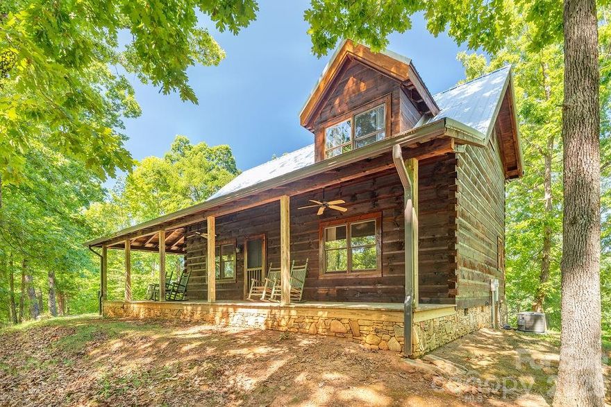 Tucked away along the edge of the South Mountains in Western North Carolina, this charming cabin on 8+ acres offering exceptional peace and natural beauty. Property is best suited for enjoyment as-is and is not intended for further development or additional structures.  A garage or outbuilding near the home would be a possibility.  The land offers the perfect balance of rustic beauty and modern comfort. Surrounded by towering hardwoods and the sounds of nature, this private retreat invites you to truly unplug and unwind. Explore your own wooded acreage or venture onto the nearby trails of the adjacent NC Game Land—outdoor adventure is right at your doorstep. Inside, the cabin welcomes you with a warm and inviting living room featuring vaulted ceilings, rich wood interiors, and a stunning floor-to-ceiling stone fireplace. West-facing picture windows fill the space with natural light and frame breathtaking sunset views each evening. Step outside onto the wraparound porch—ideal for morning coffee among the trees or relaxing evenings under a canopy of stars. The upper-level bath offers a spa-like experience with a newly updated walk-in tiled shower (2024) and a jetted tub. Thoughtful updates provide peace of mind, including a new HVAC system with Nest thermostat (2023), new well and pump (2022), and a durable metal roof (2021). An outdoor shed adds additional storage for tools and gear. Whether you’re searching for a peaceful getaway, a second home, or a full-time mountain escape, this property captures the timeless magic of life in the North Carolina mountains. Located just 20–30 minutes from Marion, Rutherfordton, Forest City, and Morganton, you’ll enjoy both seclusion and convenience. As an added bonus, walk across the street to access over 500 acres of NC State Forest protected game lands—perfect for hiking, exploring, and connecting with nature.