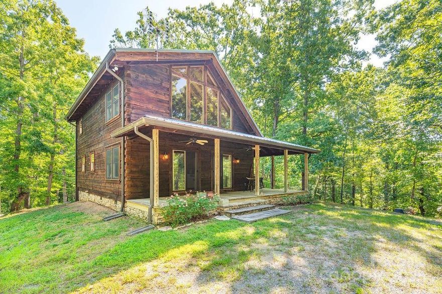 Tucked away on the edge of the South Mountains in Western North Carolina, this charming cabin on 8+ acres offers the perfect blend of rustic beauty and modern comfort. Surrounded by towering hardwoods and the sounds of nature, you'll enjoy the privacy of this natural retreat where you can peacefully unplug and unwind. Roam and enjoy this property and trails of the adjacent state park.  The cabin features: a Living Room with vaulted ceiling, warm wood interiors, a floor to ceiling stone fireplace, and west facing picture windows with spectacular sunset views. Step outside onto the wraparound porch to enjoy a beverage among the trees and evenings under a blanket of stars. The Upper Bath offers a new walk-in tiled shower (2024) and a jet tub. A new HVAC with Nest Thermo (2023), new well and pump (2022), metal roof (2021) and outdoor shed. Whether you’re looking for a quiet getaway, 2nd home, or a full-time mountain escape, this cabin embodies the timeless magic of life in the North Carolina mountains. Walk across the street to 500 acres of NC State Forest protected gamelands. (Property is 20-30 Minutes central to Marion, Rutherfordton, Forest City & Morganton).