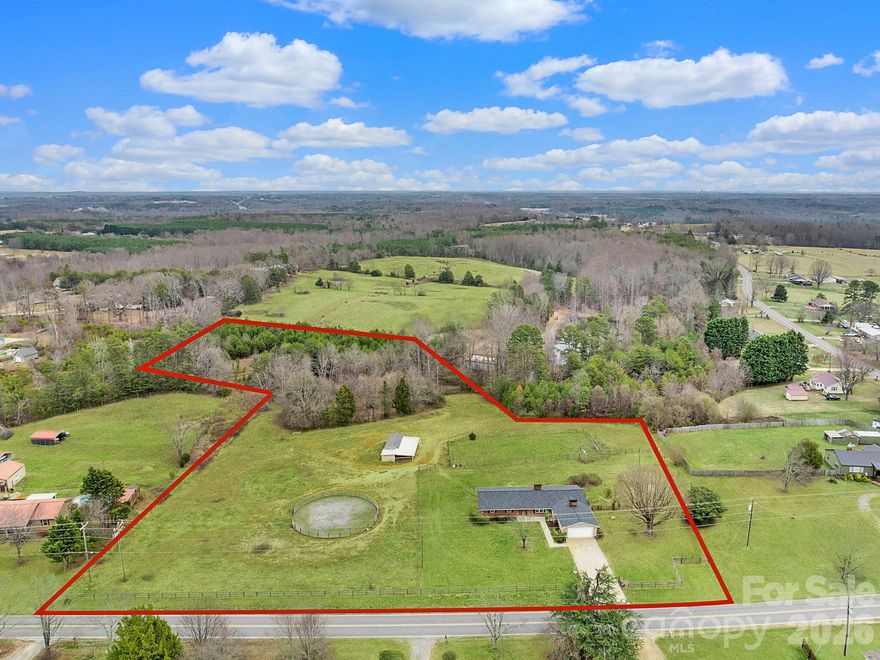 Whether you envision a peaceful self-sustaining farming homestead, a functional equestrian estate, or a private family compound, this 6.25-acre property offers the opportunity. Perfectly blending rural charm with modern accessibility, you’ll enjoy a serene landscape of fenced pastures and woods just minutes from the shopping and dining of Forest City/Spindale and only 11 minutes from Tryon International Equestrian Center.  This sprawling 2,202 sq. ft. main level living ranch features a new roof (installed four years ago) and a versatile floor plan. At its heart is a massive family room with vaulted ceilings, built-in bookcases, and a wood-burning fireplace. A second sun-drenched living area offers a mid-century modern vibe with a gas fireplace and seamless flow into the kitchen and dining spaces. A flexible adjacent room serves perfectly as a home office or formal dining area. Recently refinished hardwood floors in living room and bedrooms, freshly painted interior and new water heater (2022), this is a well-built and well-maintained home. Gated driveway. Expansion Potential: The unfinished basement with interior/exterior access is a blank canvas, already professionally waterproofed with a wall seal, dehumidification system, and sump pump. It offers an ideal footprint for a second living suite, income producing rental unit, or hobby space. With over six acres, the land itself provides the rare potential to subdivide or build additional homes. (buyer should check with the County for permitted uses) Ready for your horses or farm animals, the property includes a 2-stall barn with a dedicated feed/tack room; additional overhang shelters for livestock; a professional round pen featuring graded bluestone mix footing; Experience the best of country living without sacrificing convenience. This is more than just a home; it’s a multi-use investment with endless possibilities.